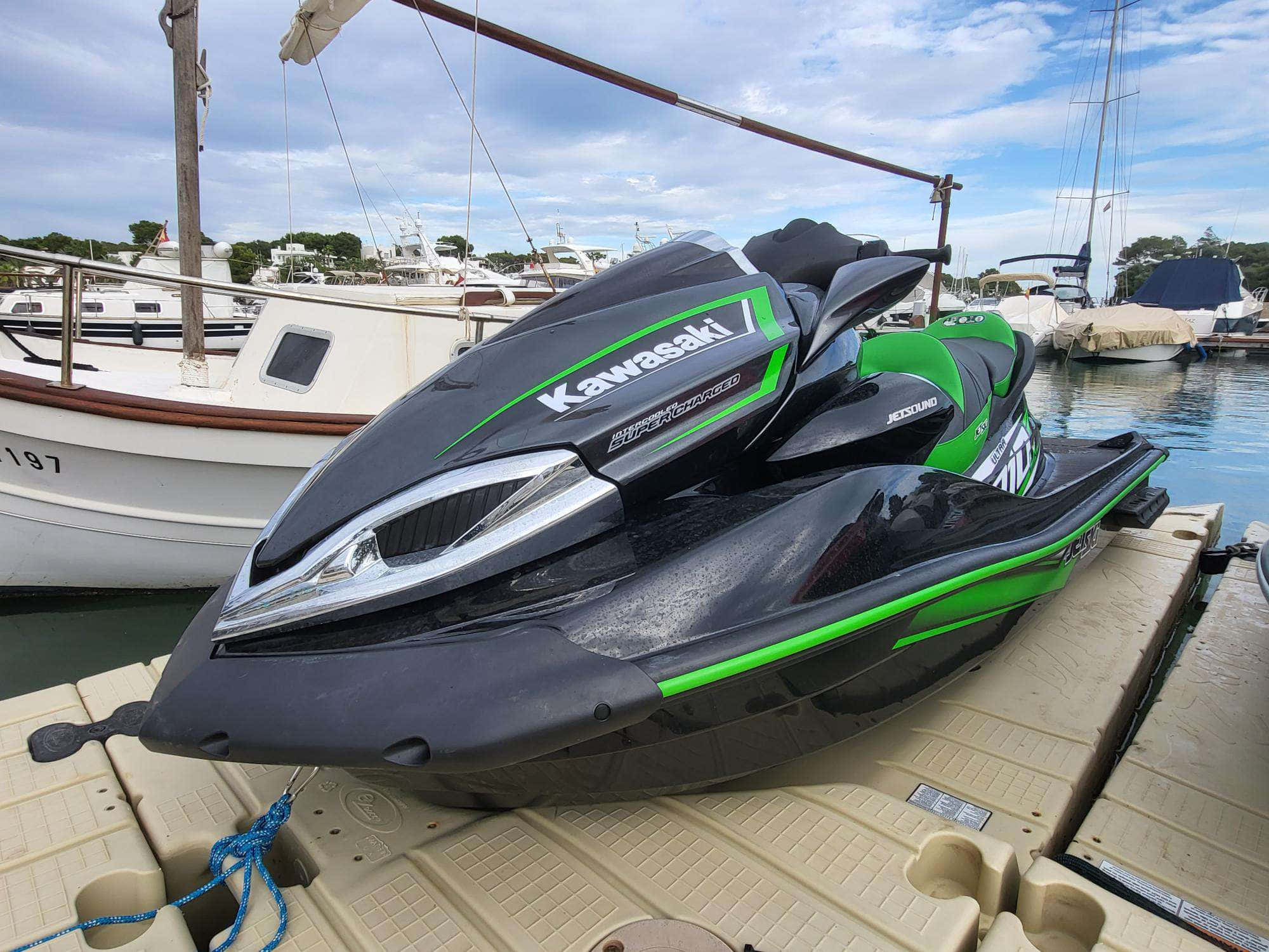 川崎黑綠色摩托艇 壁紙 — 一艘時尚的黑色和綠色 Kawasaki 水上電單車停靠在碼頭邊，旁邊有船隻，天空部分多雲。