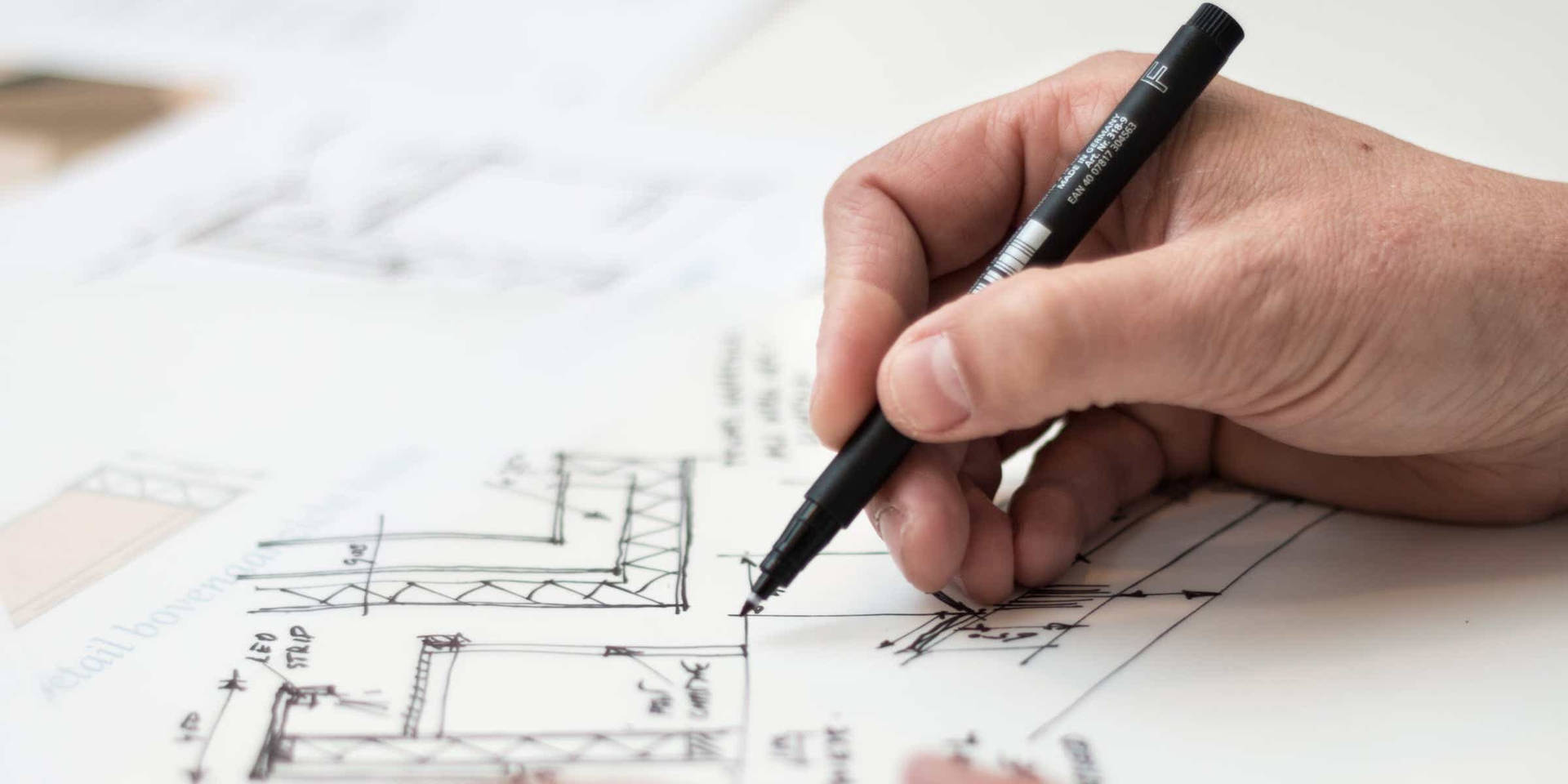 手用黑色馬克筆在白紙上繪製建築計劃。
