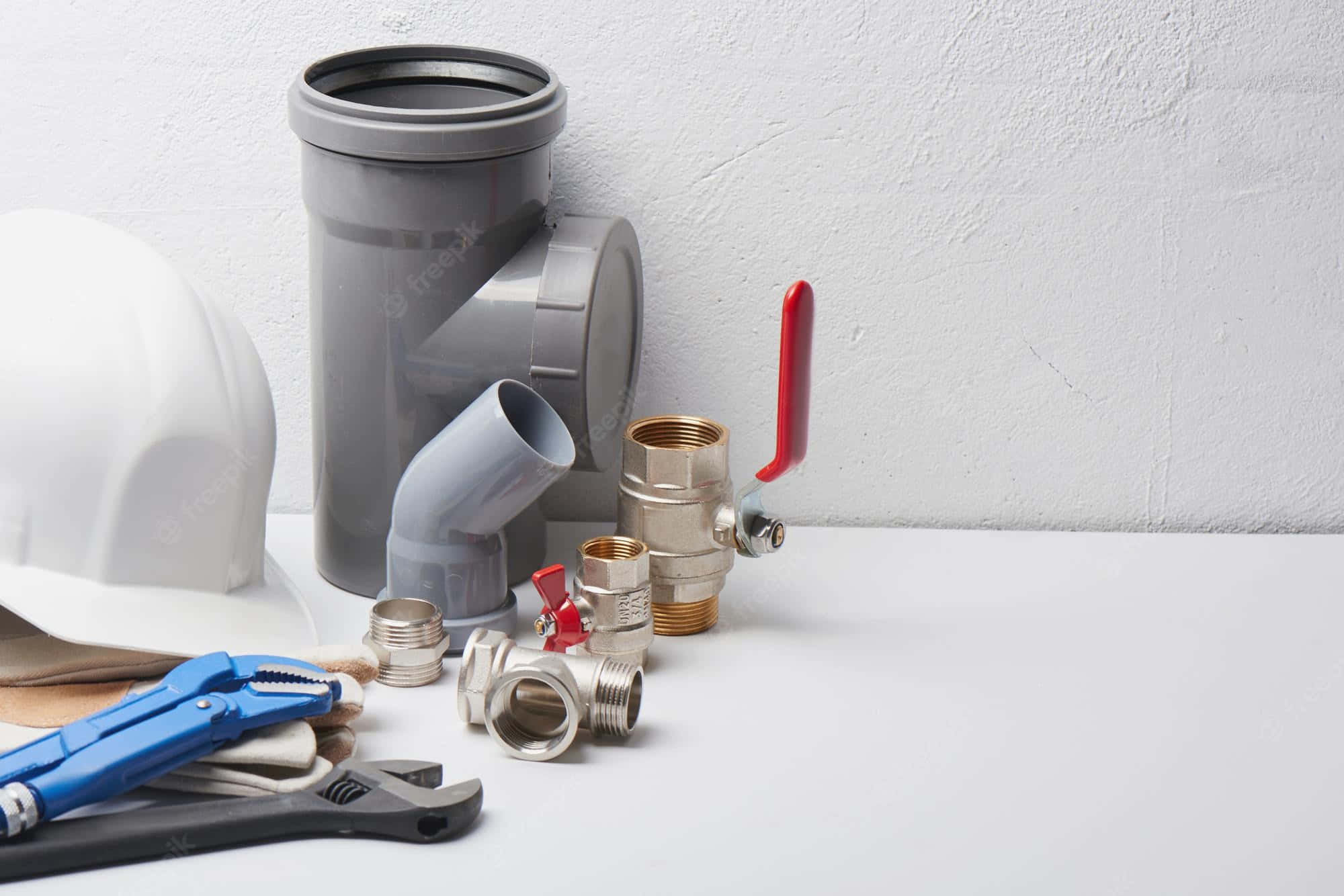 工程師與 Plumbing 配件及工具 壁紙 — 一系列水喉工具和管道整齊地排列在白色表面上，背景為有紋理的牆壁。