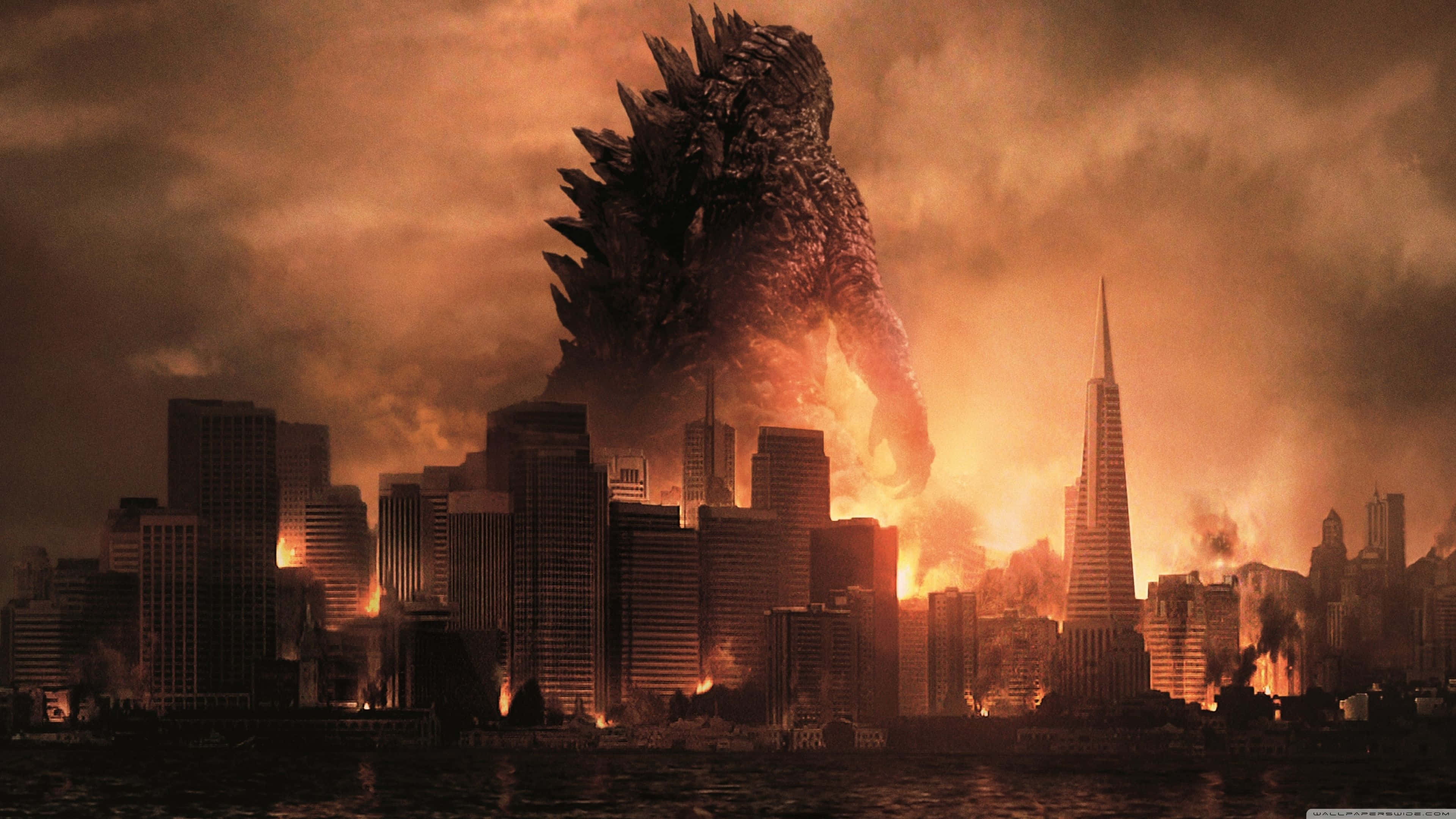 Burning Godzilla 桌布 壁紙 — 巨型哥斯拉聳立在夕陽下燃燒的城市景觀之上，火焰和煙霧從被摧毀的摩天大樓中升起。