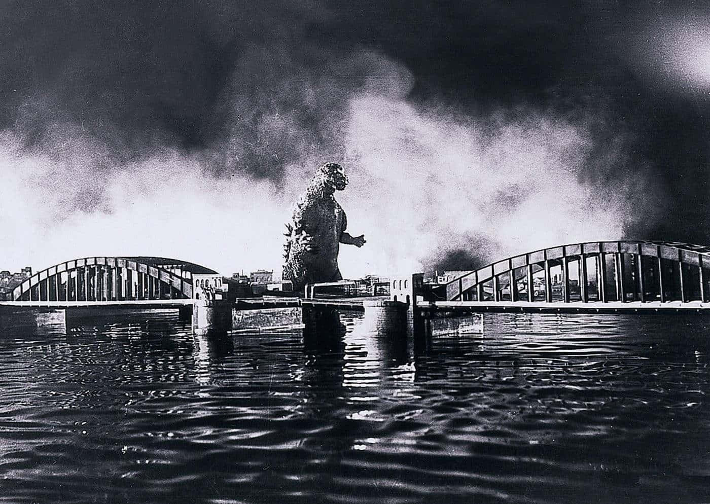 Classic Godzilla 桌布 壁紙 — 巨型怪獸哥斯拉站在水中，周圍是斷橋，身後濃煙滾滾，形成戲劇性的黑白場景。