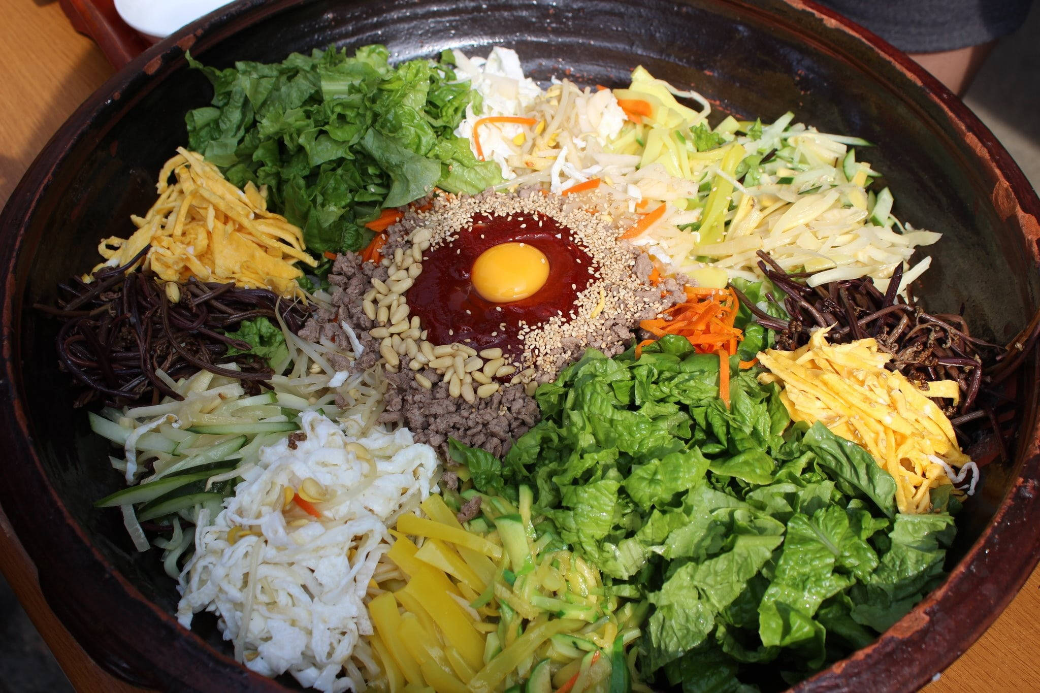 巨型拌飯盤 壁紙 — 色彩繽紛的韓式石鍋拌飯，上面放有生蛋黃和芝麻。