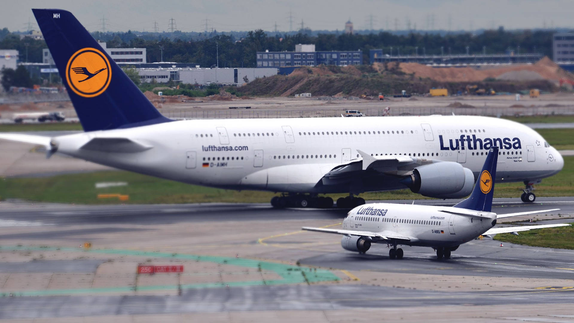 兩架漢莎航空飛機在機場停機坪，背景有跑道和建築物。