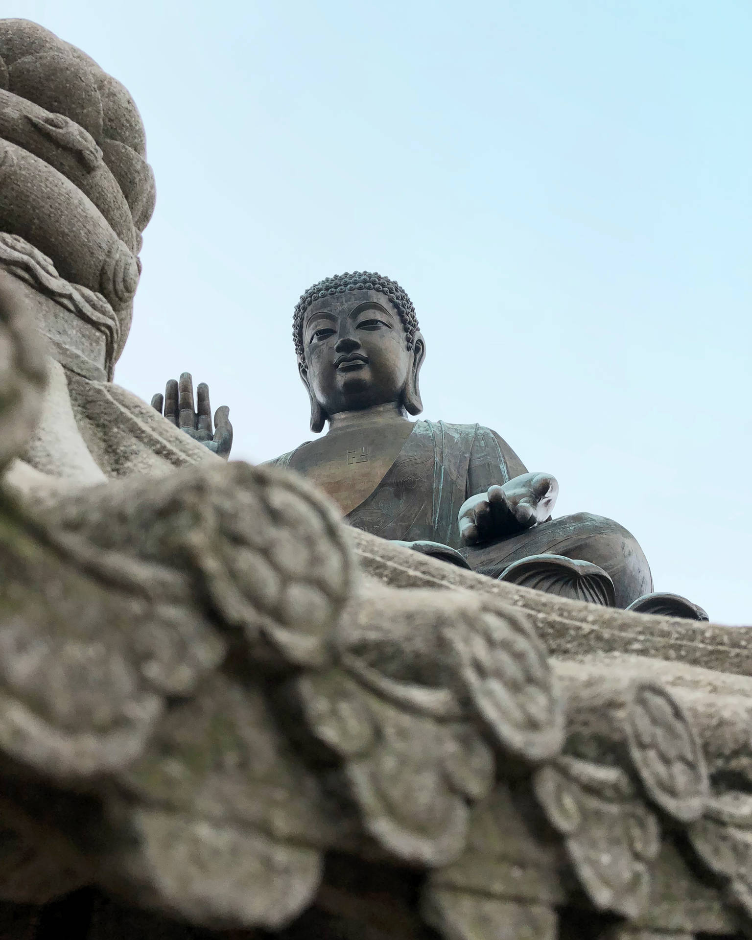 一座大型青銅佛像坐在石造建築上，天空蒼白。