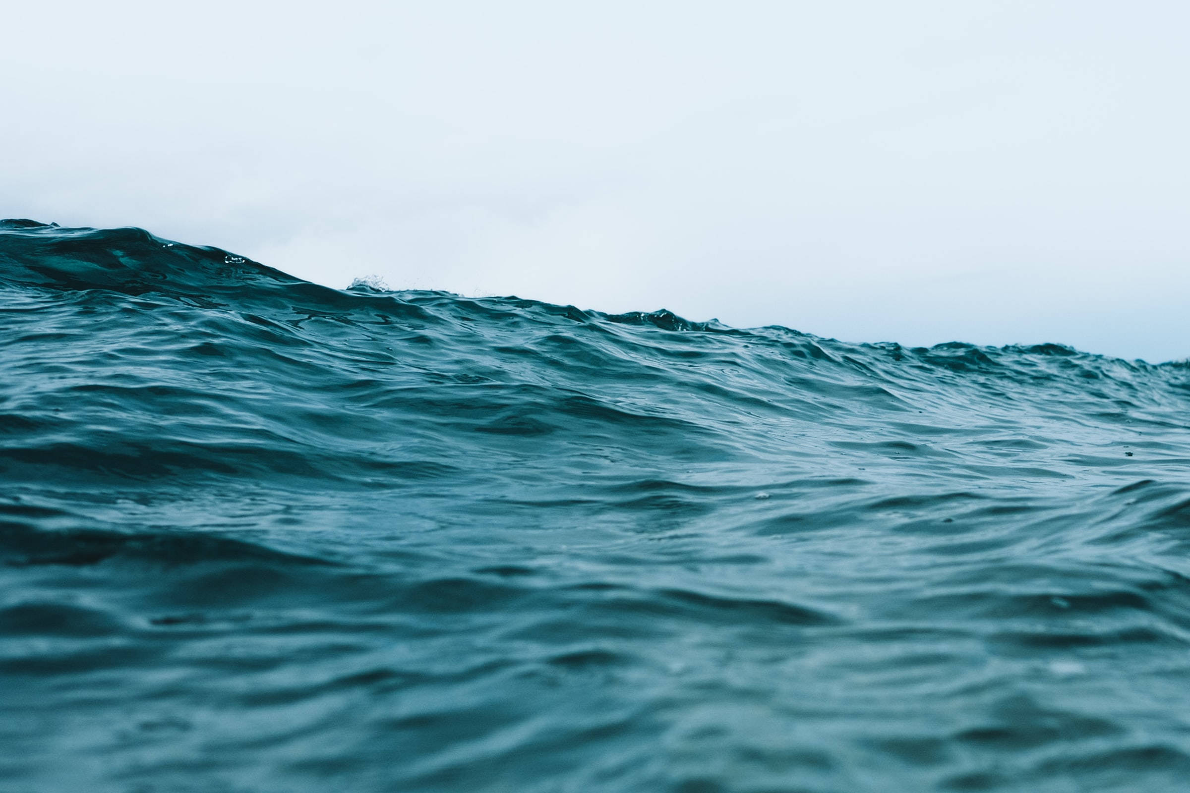 巨大的海洋藍色海浪 壁紙 — 從低角度觀看，在陰天天空下洶湧的青綠色海浪翻騰。