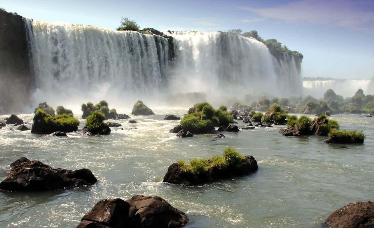 3d Waterfall 桌布 壁紙 — 巨大的瀑布從懸崖傾瀉而下，流入下方湍急的河流，霧氣升騰，綠色植被攀附在深色岩石上。