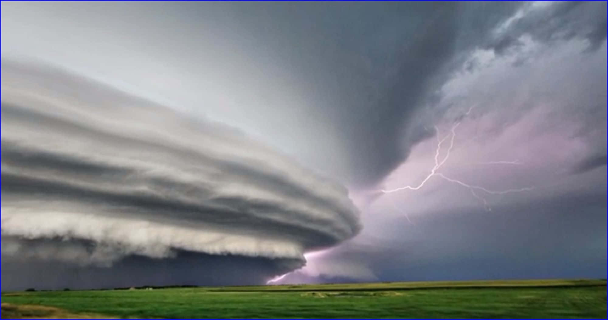 Thunderstorm 桌布 壁紙 — 巨大的風暴雲籠罩著一片綠色田野，閃電在黑暗的天空中劃過。