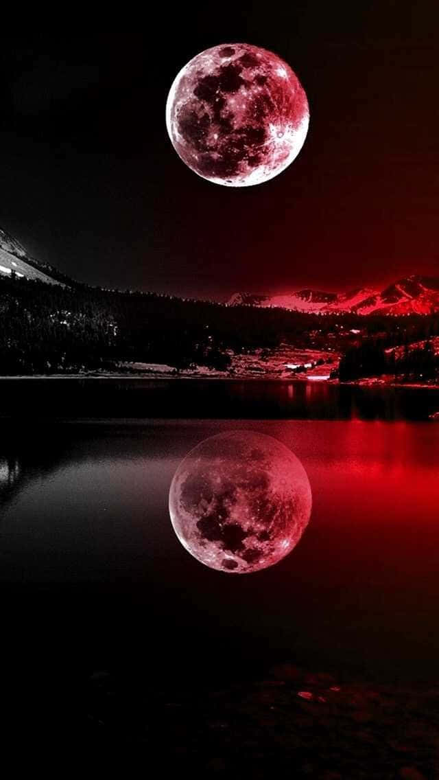 巨大紅色夜空月 壁紙 — 血紅色的月亮懸掛在積雪的山峰上，在黑暗的天空下完美地倒映在平靜的湖面上。