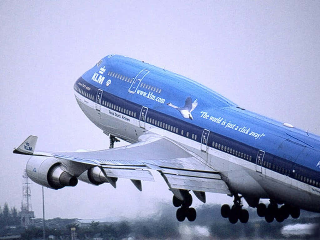 藍色KLM波音747飛機降落，起落架清晰可見，背景為城市。