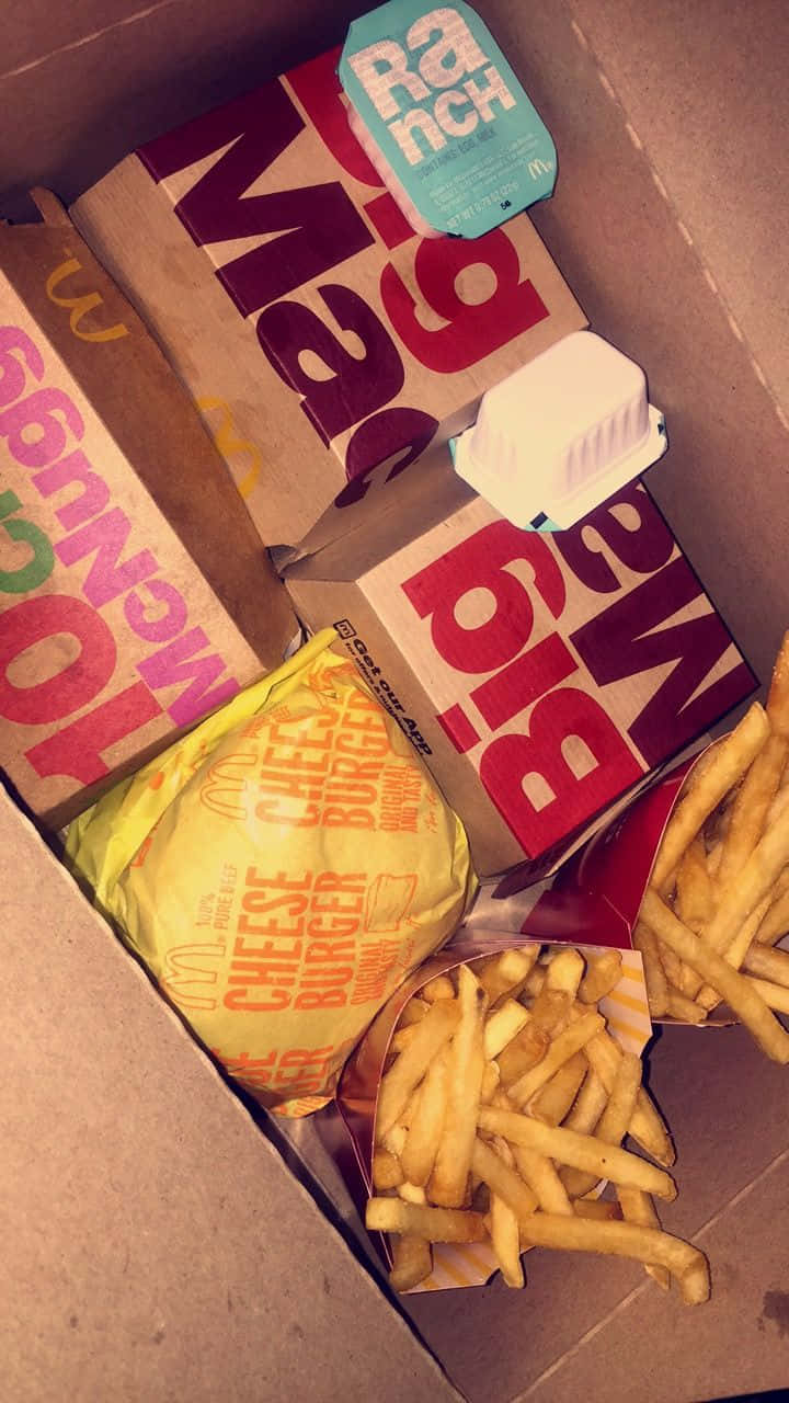 巨無霸與薯條的餐盒 壁紙 — 從上方俯瞰一個裝滿麥當勞食物的紙箱，包括芝士漢堡、薯條和一個田園醬包。