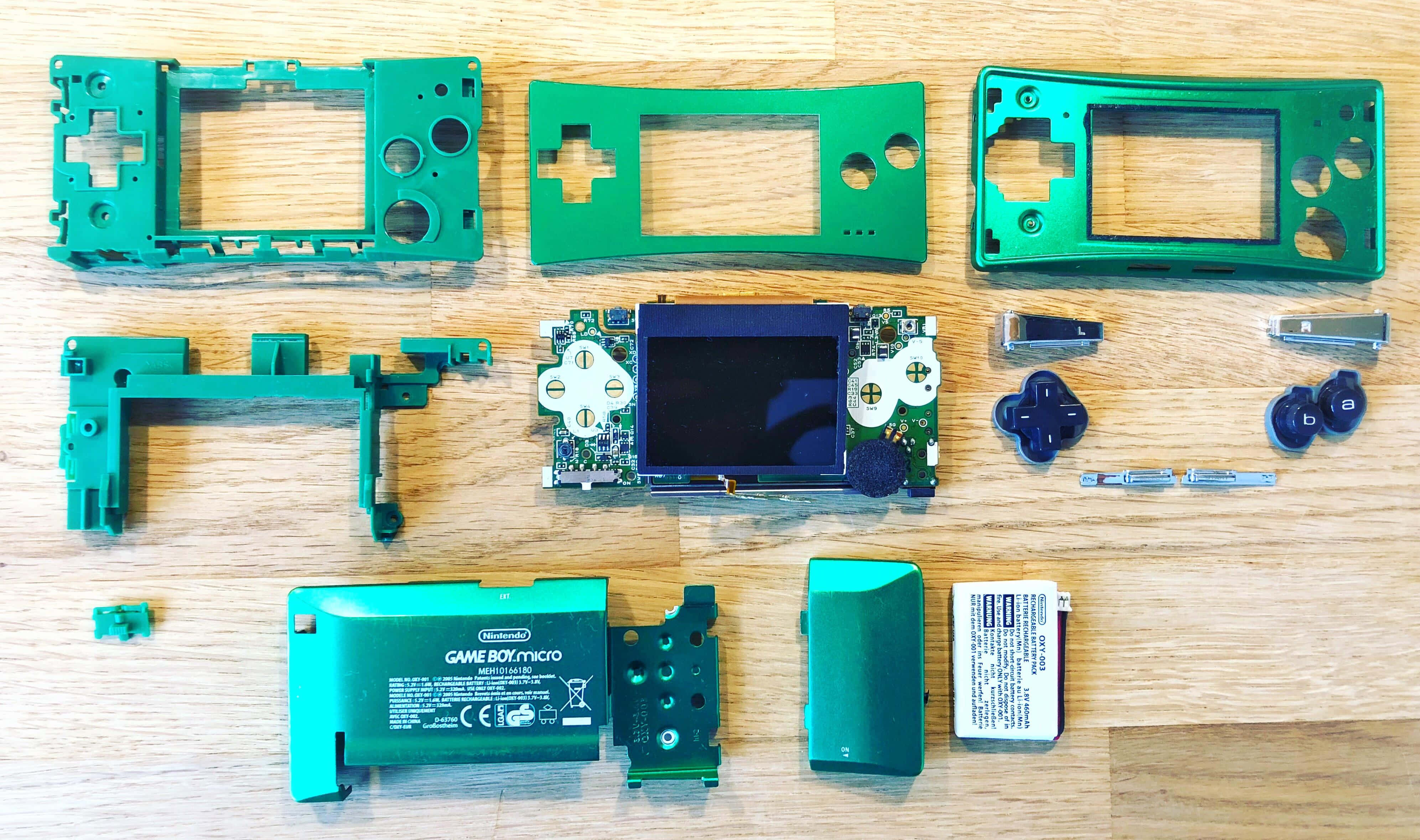 4K Gaming Consoles 桌布 壁紙 — 已拆解的綠色 Nintendo Game Boy Micro，內部零件整齊排列在木質表面上。