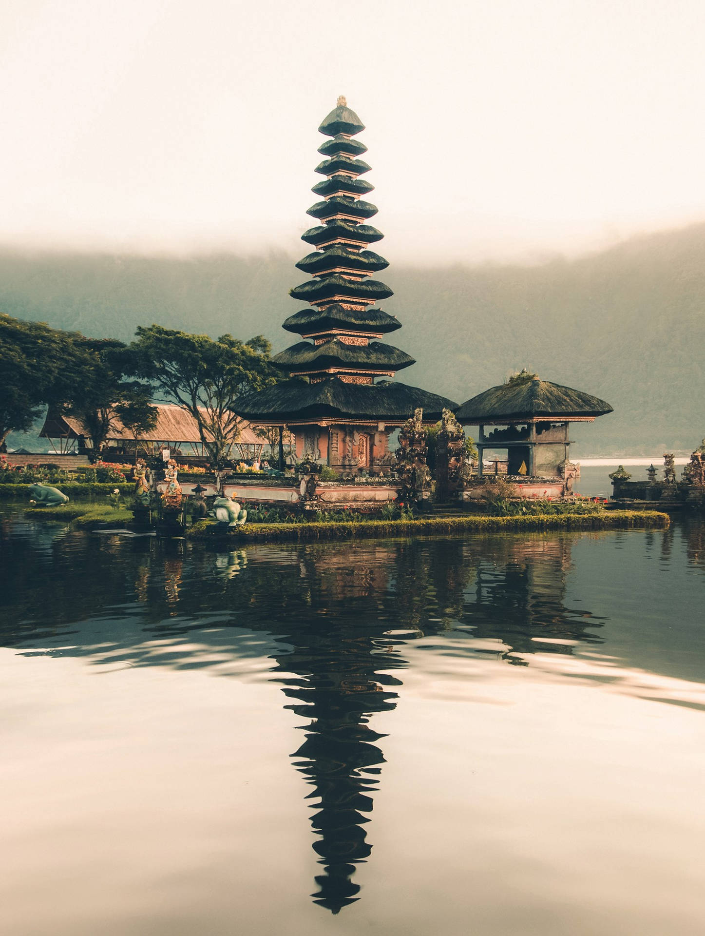 峇里島寺廟倒映在平靜的湖中，背景有霧氣繚繞的山巒