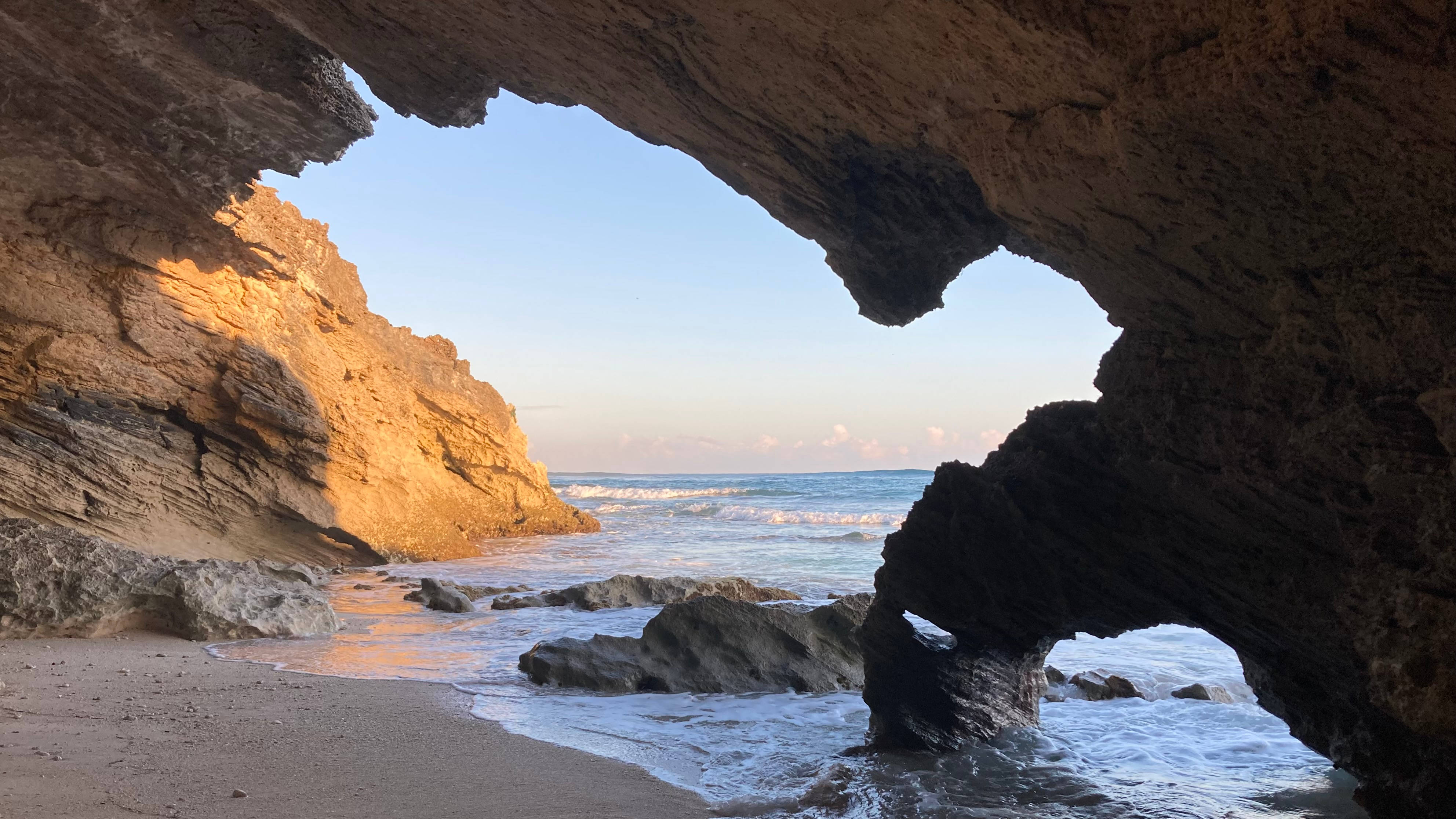 巴哈馬島上的洞穴 壁紙 — 陽光穿過天然岩石拱門，框住沙灘和碧綠海洋，正值黃金時刻。