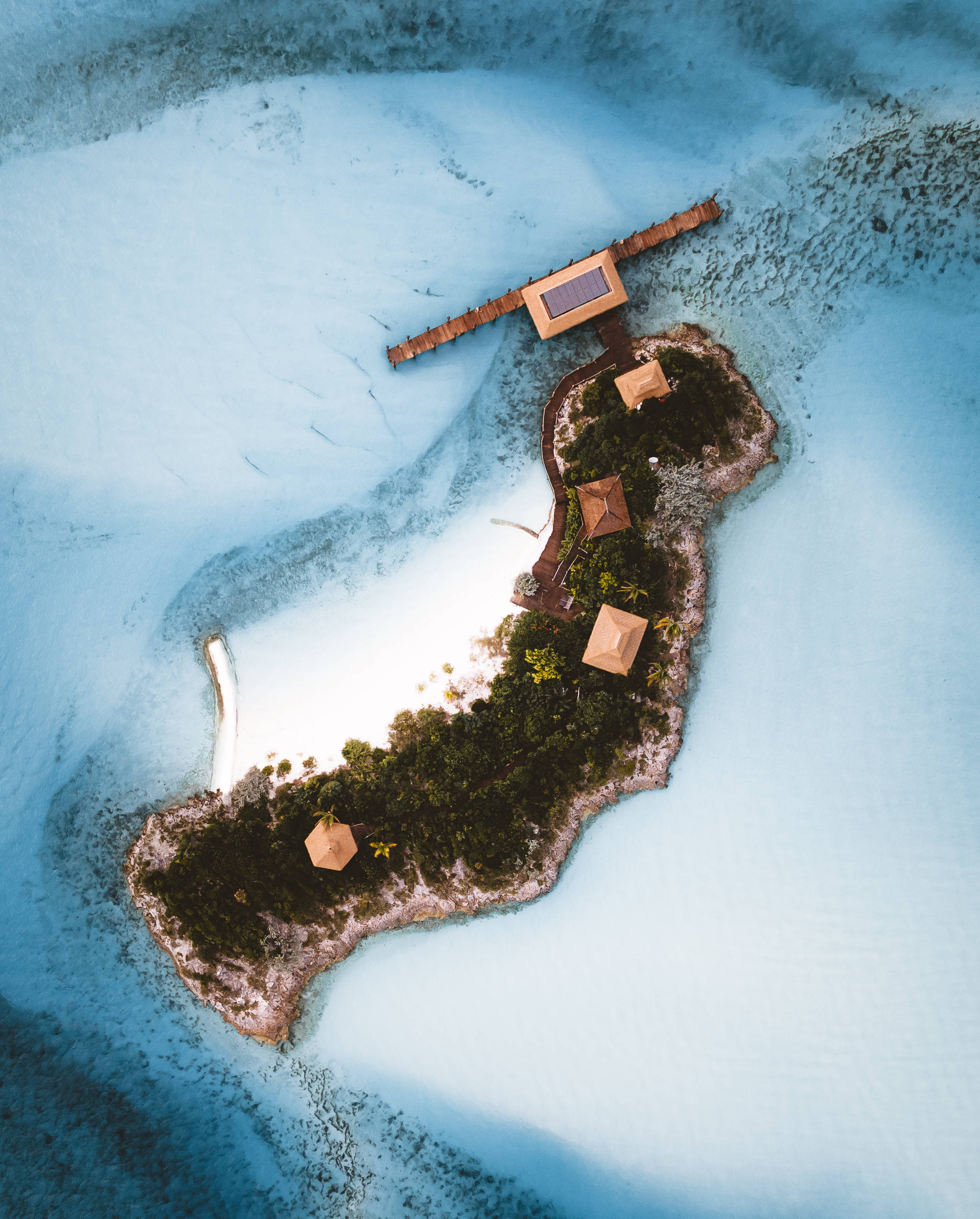 巴哈馬島空拍視角 壁紙 — 熱帶島嶼的鳥瞰圖，島上有木製別墅和一個太陽能板碼頭，周圍是清澈見底的碧綠海水。