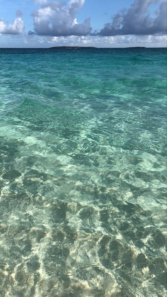 在多雲的天空下，清澈的碧綠海水，可見沙子和輕柔的波浪。
