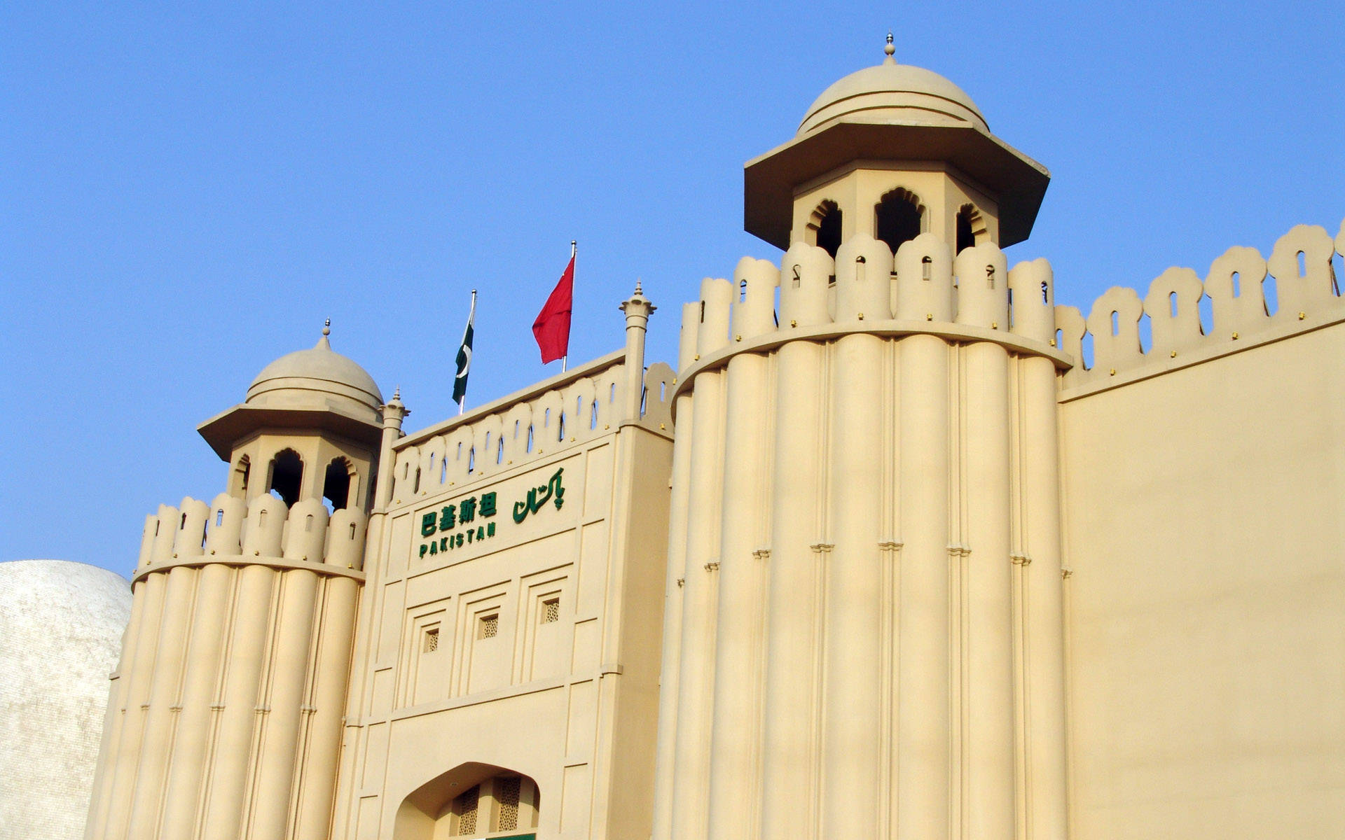 巴基斯坦拉合爾堡 壁紙 — 一座宏偉的米色巴基斯坦政府建築，擁有圓頂塔樓和旗幟，背景是晴朗的藍天。