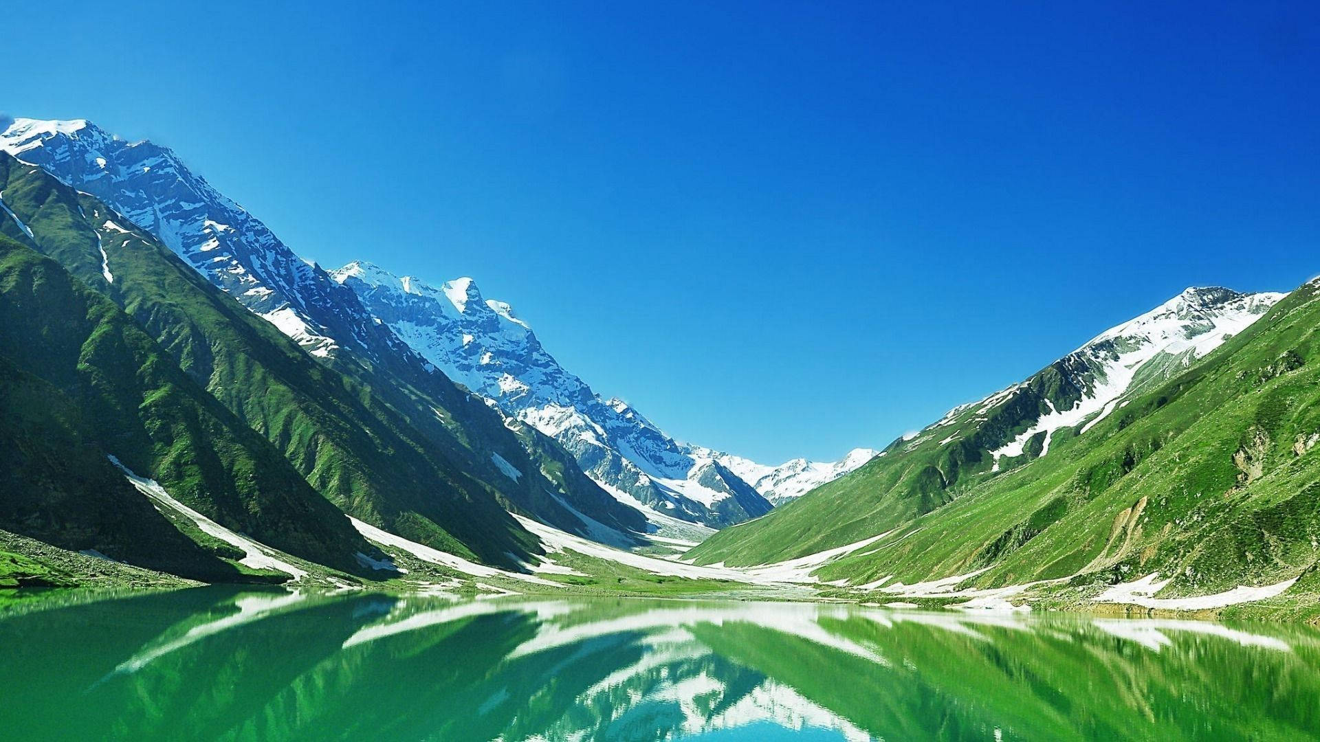 巴基斯坦自然風光 壁紙 — 純淨的高山湖泊倒映著白雪覆蓋的山峰，藍天白雲下，四周環繞著鬱鬱蔥蔥的綠色山坡。