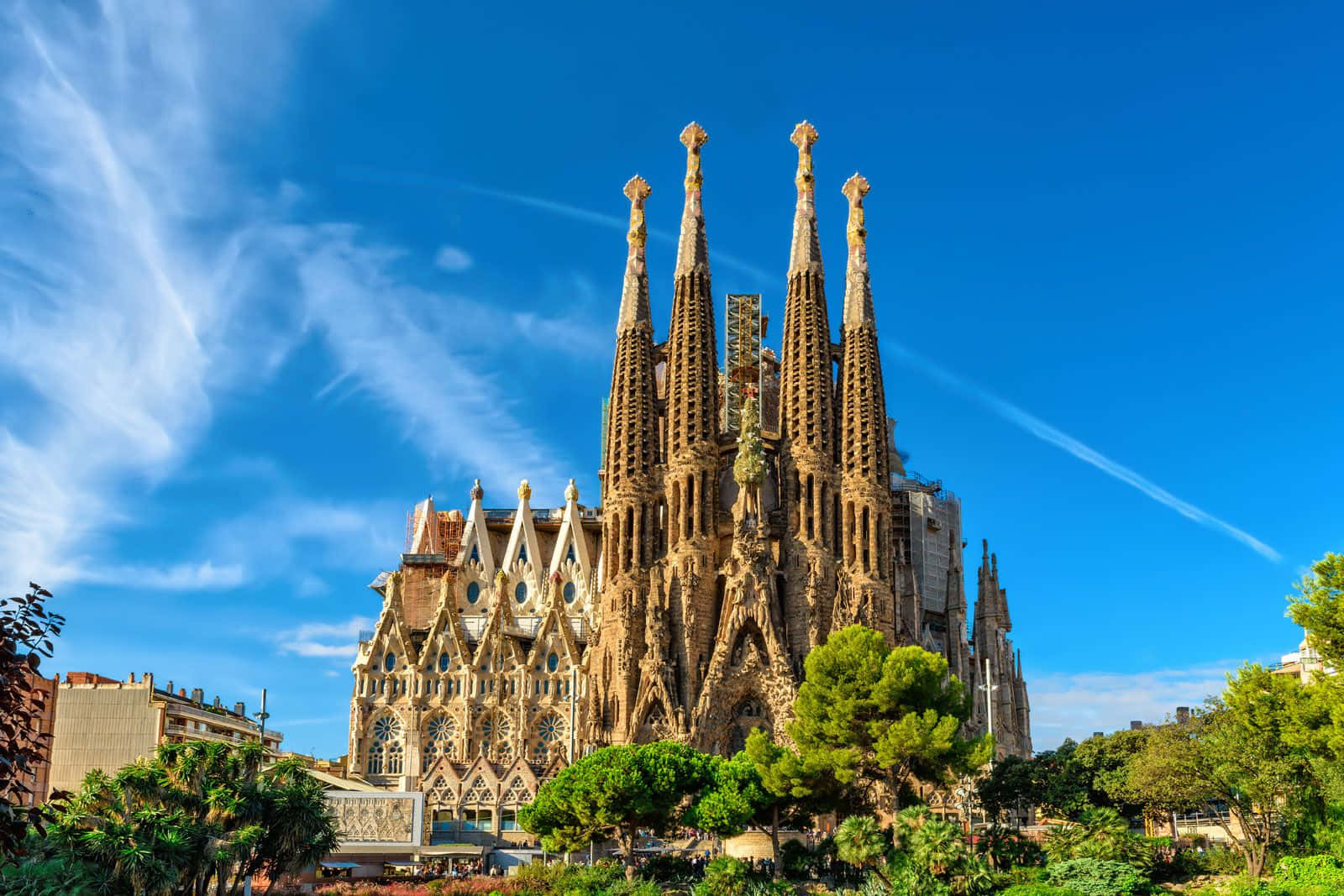Barcelona 桌布 壁紙 — 巴塞隆拿的聖家堂在蔚藍天空、縷縷白雲和腳下翠綠樹木的襯托下，雄偉地聳立。