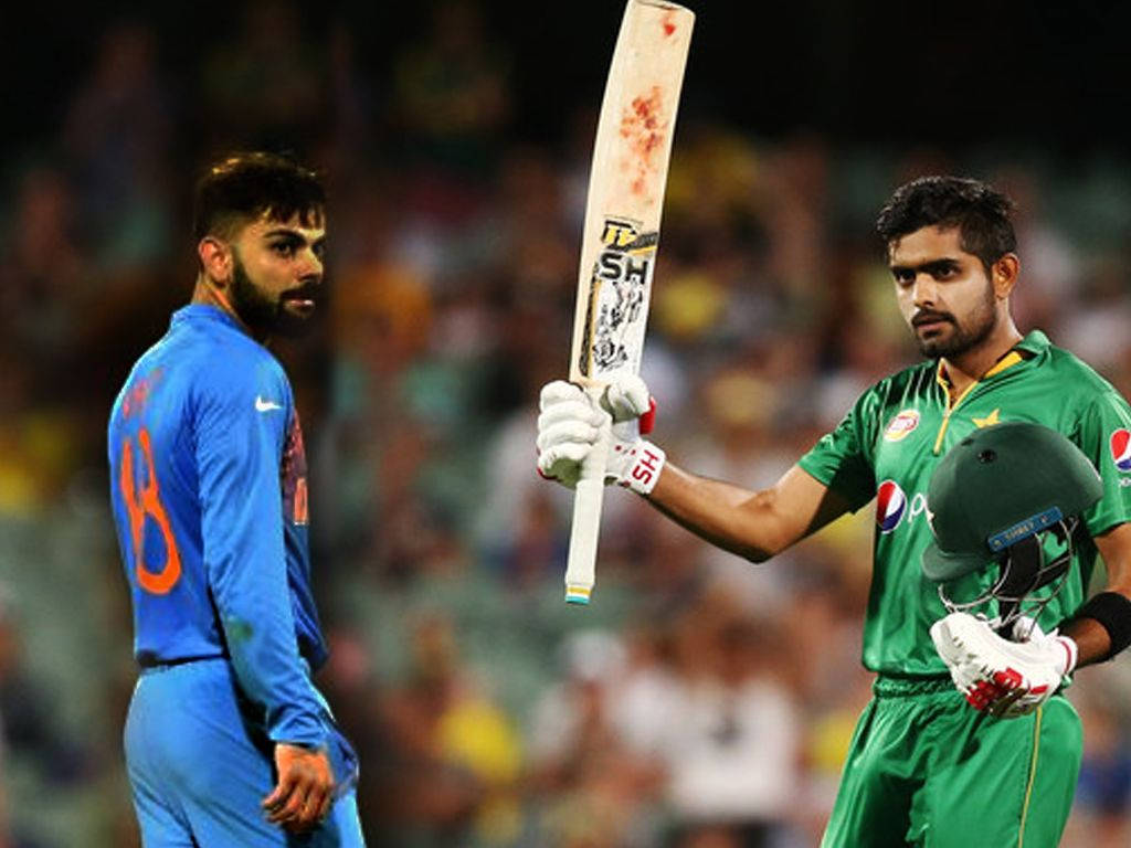 巴巴爾·阿зам與 Kohli 合影 壁紙 — 兩名身穿綠色和藍色球衣的板球運動員在夜間對峙，其中一人手持染血的球棒。