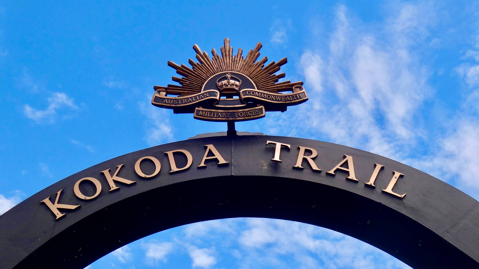 黑色拱門，金色Kokoda Trail文字和軍事徽章，藍天背景