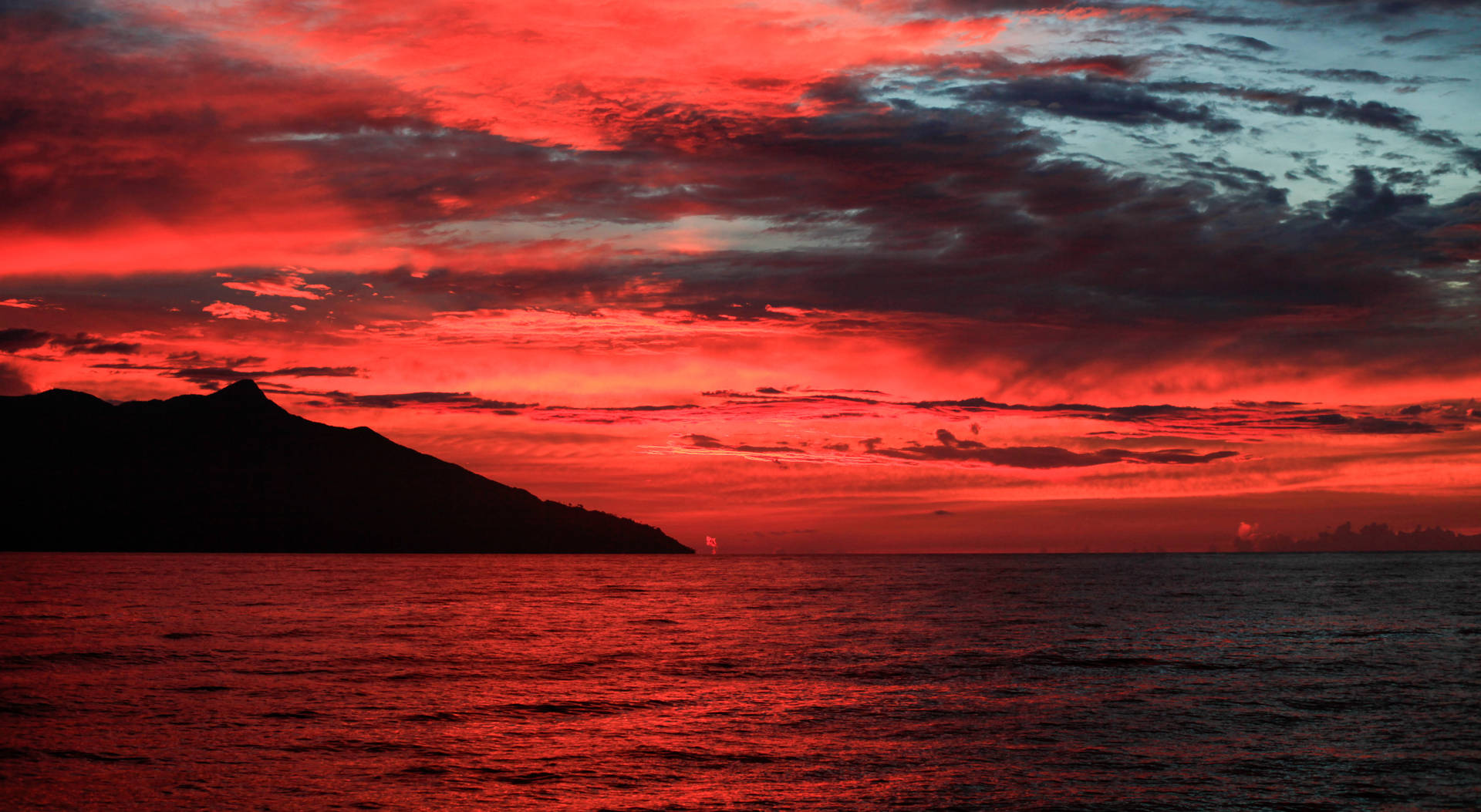 海洋上空戲劇性的紅色夕陽，遠方有山脈輪廓。