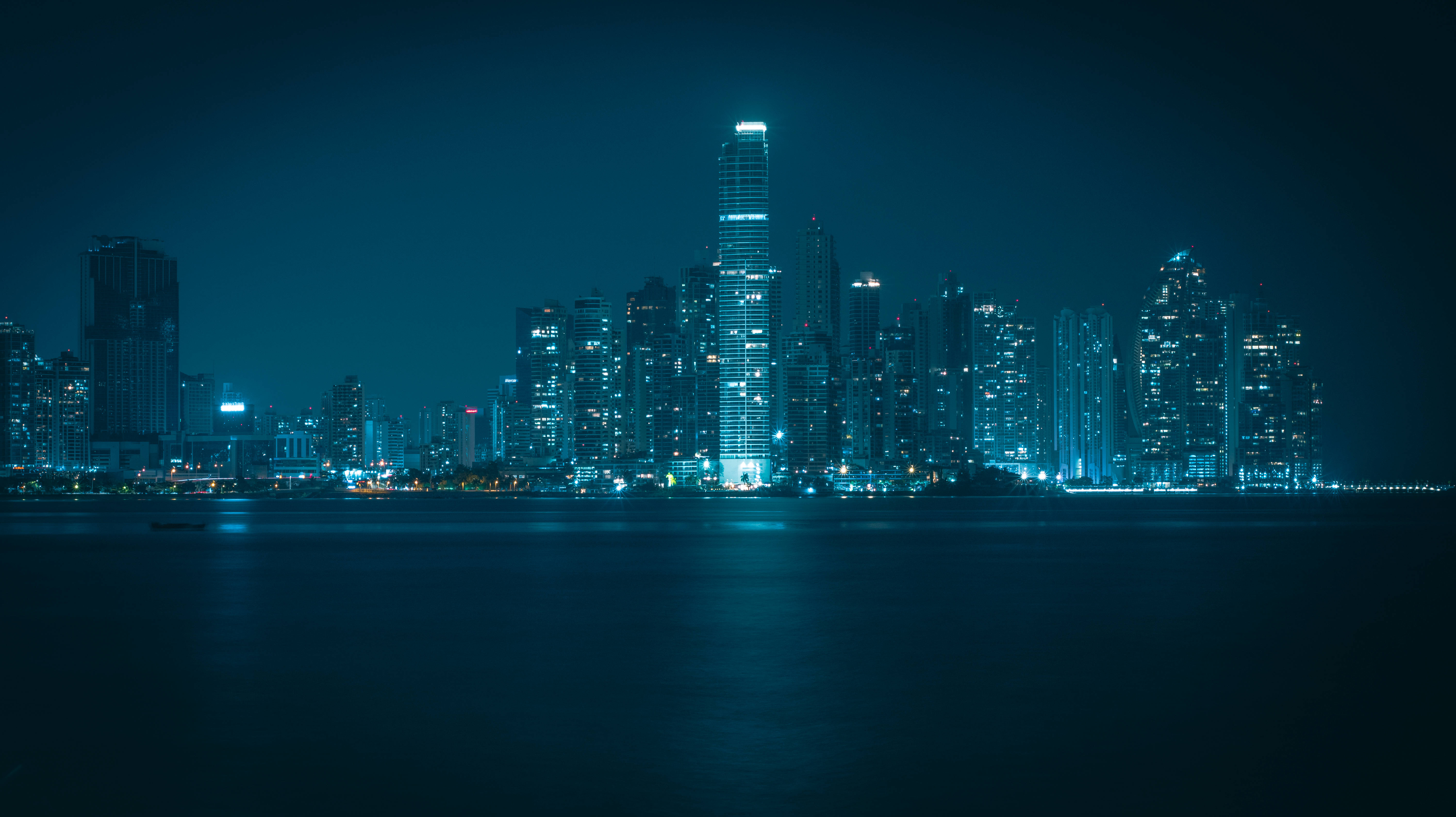 巴拿馬夜景 壁紙 — 寧靜的夜景城市景觀，在深藍色天空下，發光的摩天大樓倒映在平靜的水面上。