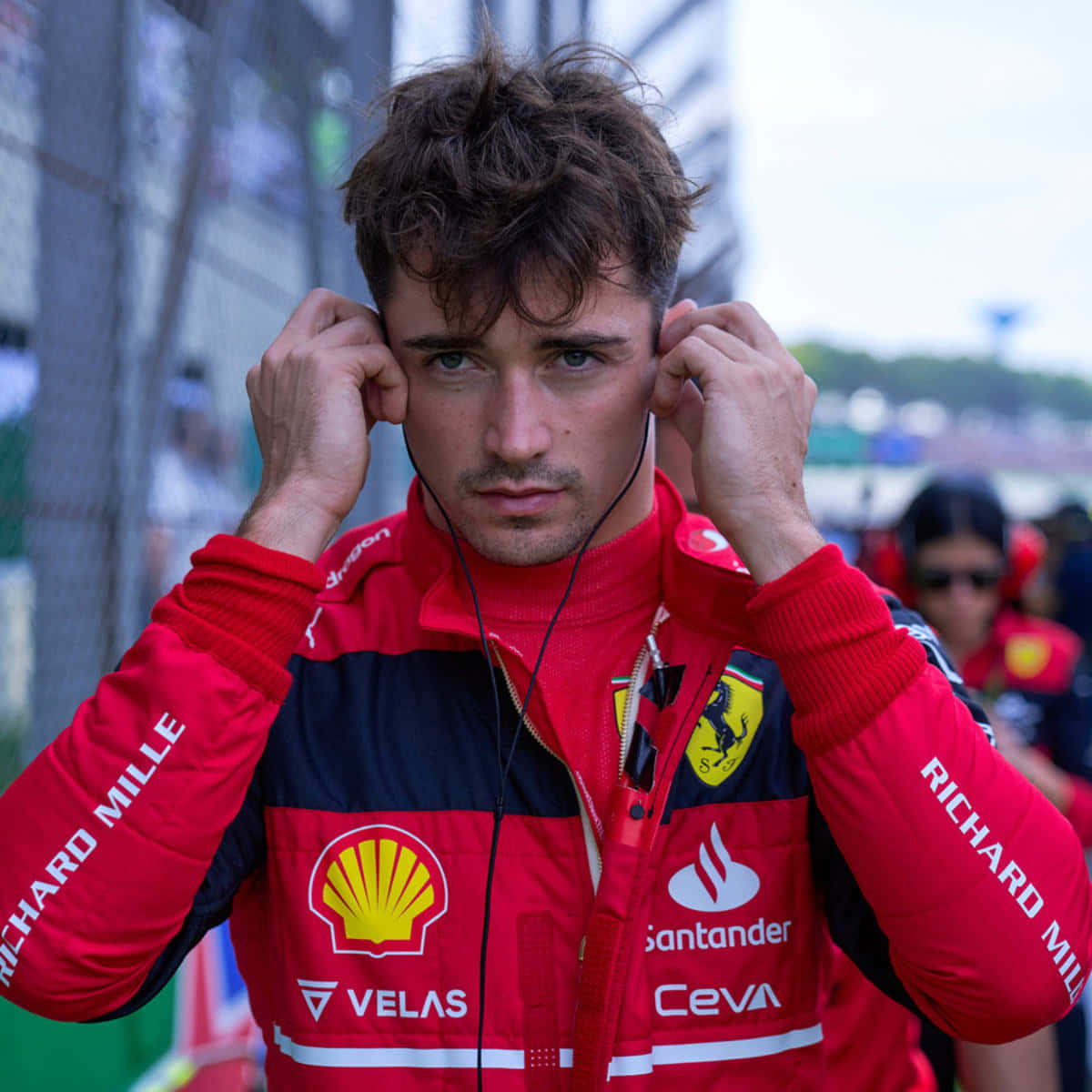 F1車手穿著紅色法拉利裝備在賽道上調整耳機。