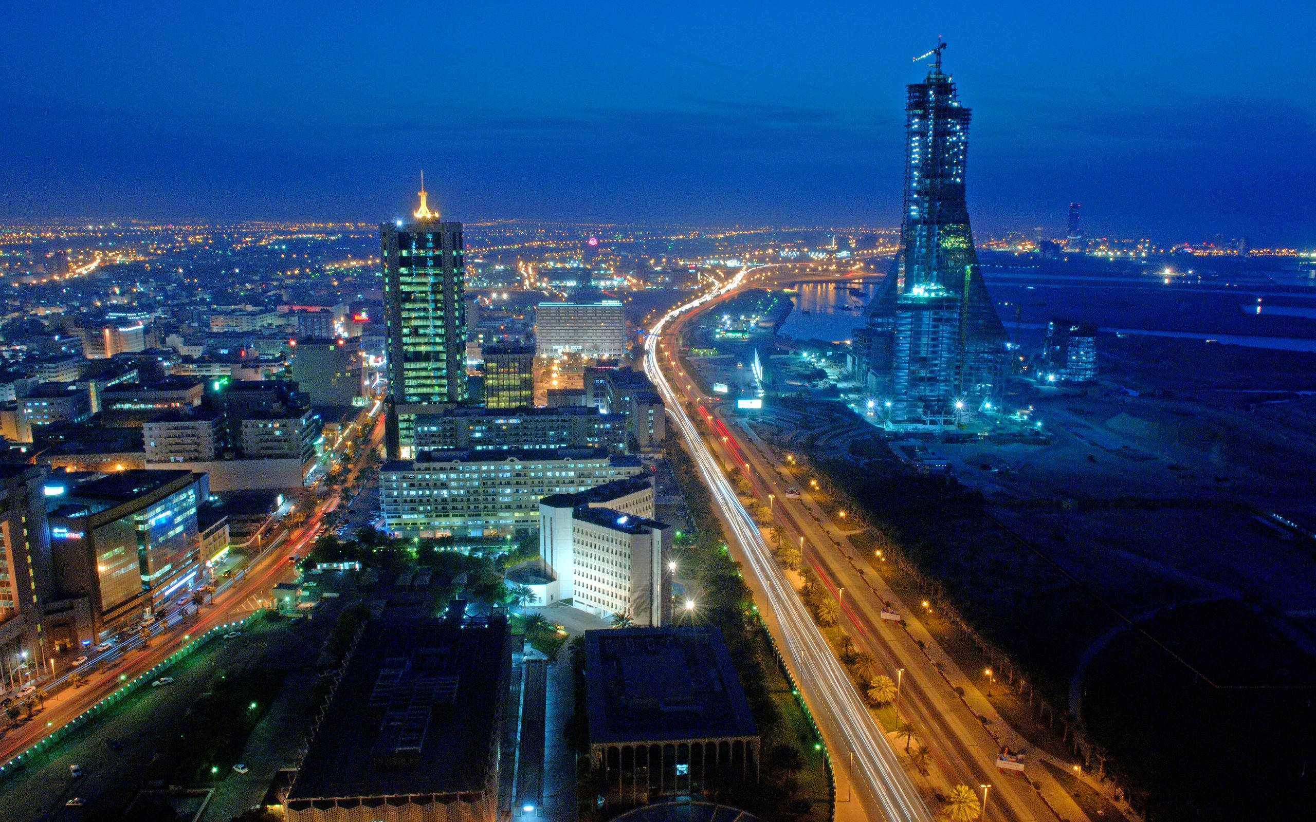 巴林夜景 壁紙 — 充滿活力的城市景觀的空中夜景，閃爍的摩天大樓和蜿蜒道路上交通留下的光跡。