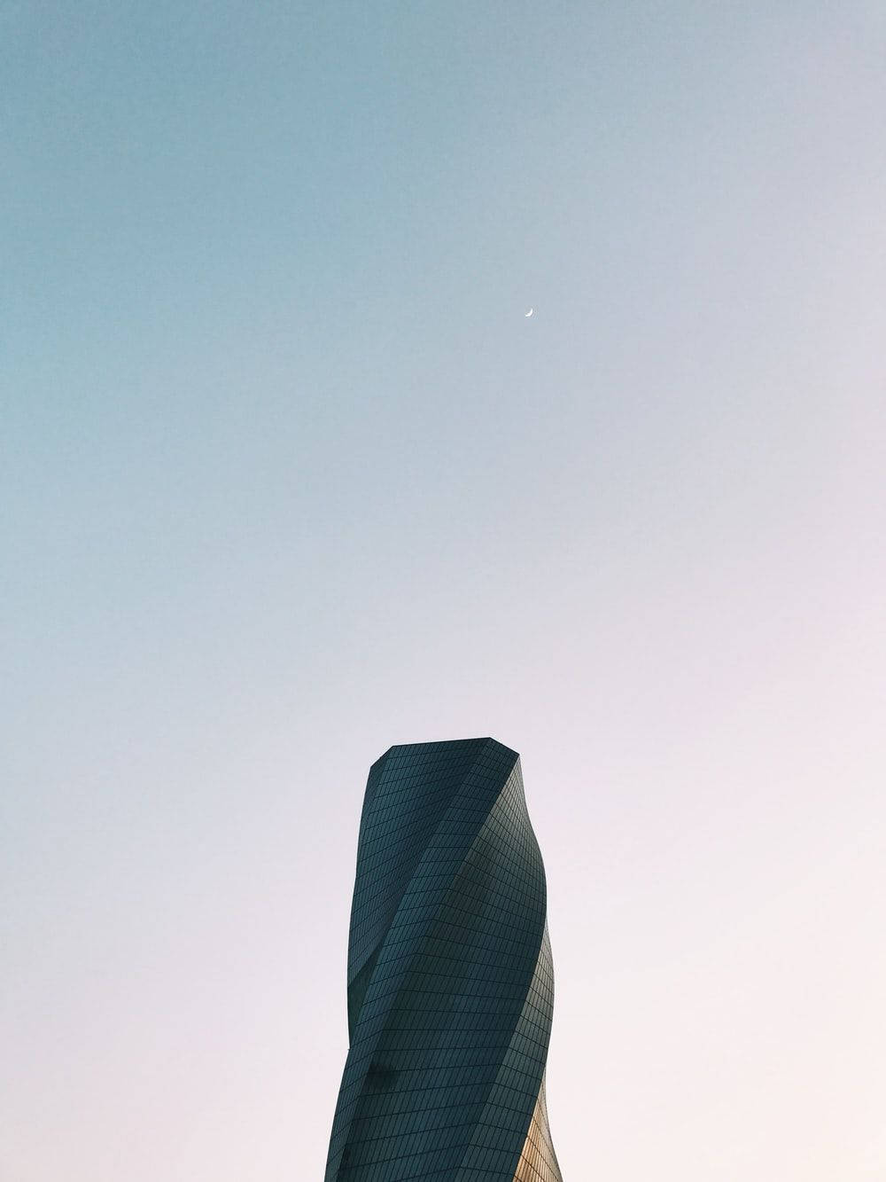 巴林聯合大樓 壁紙 — 一座時尚扭曲的摩天大樓在柔和漸變的天空中升起，上方可見一彎新月。