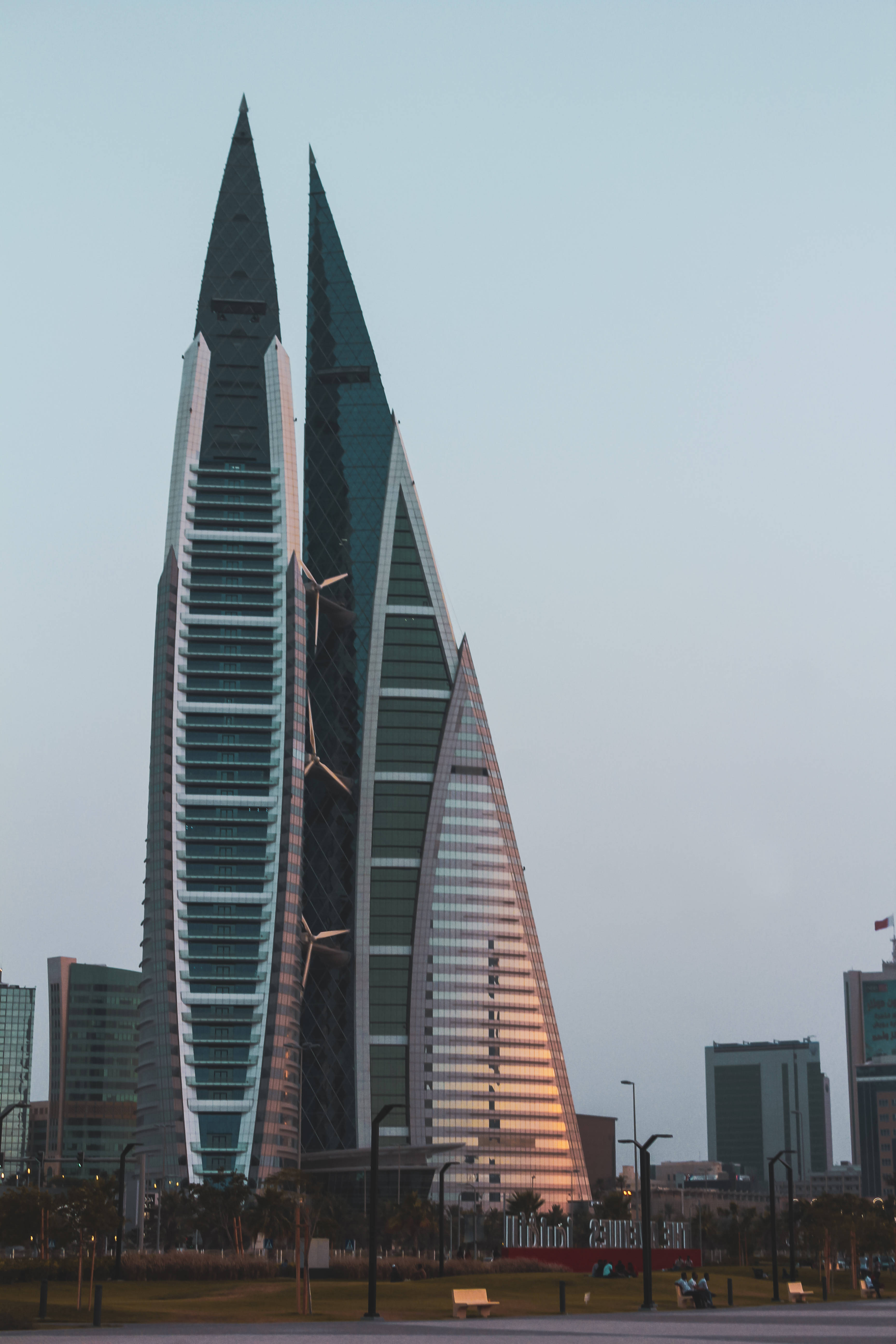 巴林高樓建築 壁紙 — 兩座標誌性的帆形摩天大樓在蒼白的天空下升起，玻璃外牆上閃爍著溫暖的日落餘暉。