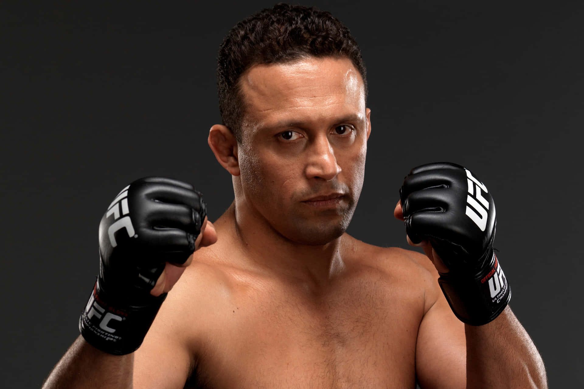 一位赤裸上身的男性MMA拳擊手，戴著黑色UFC手套，凝視著鏡頭。