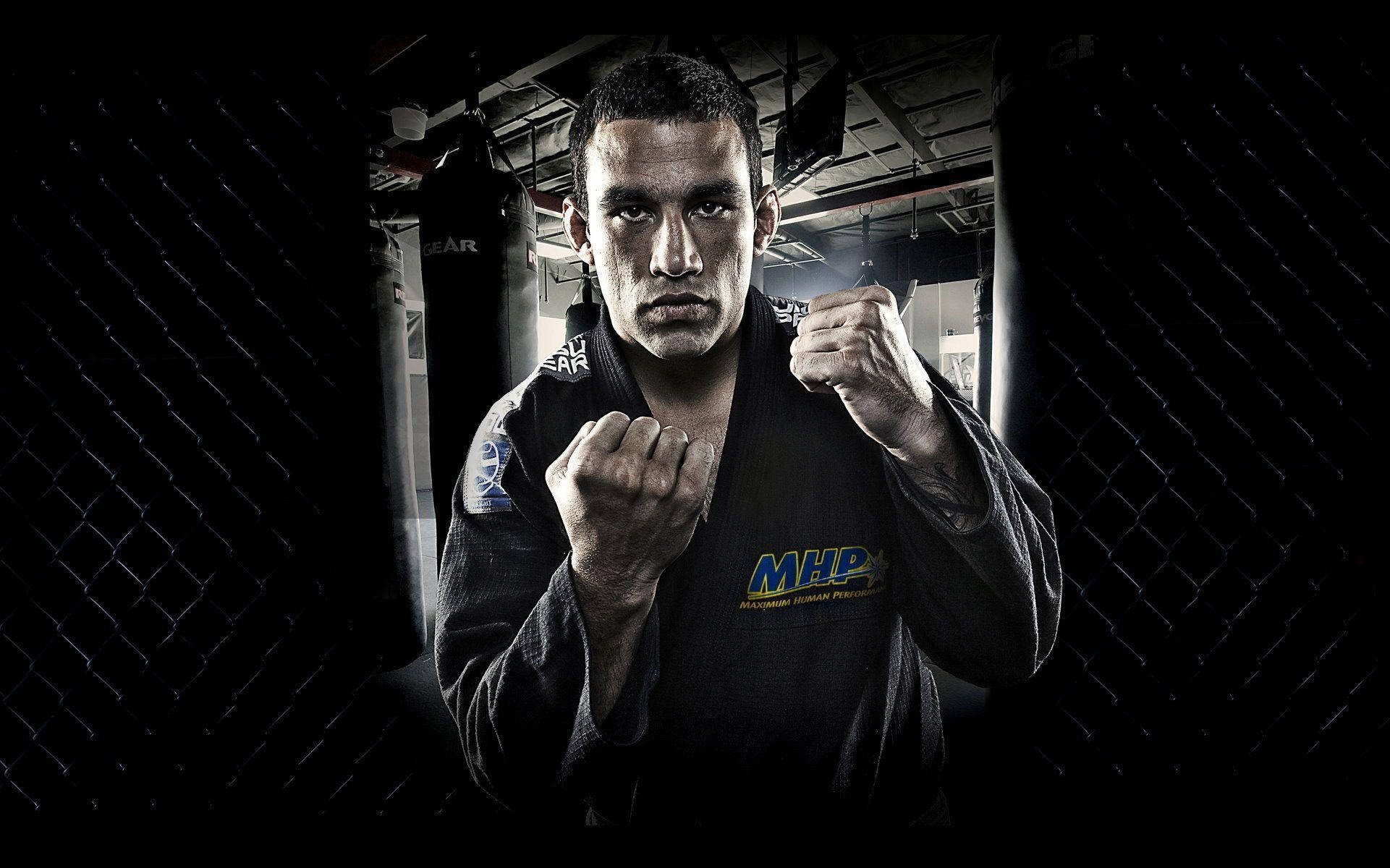 巴西混合格鬥選手 Fabricio Werdum 壁紙 — 一位專注的混合武術家穿著黑色道服，站在光線昏暗的籠子裡，舉起拳頭準備戰鬥。