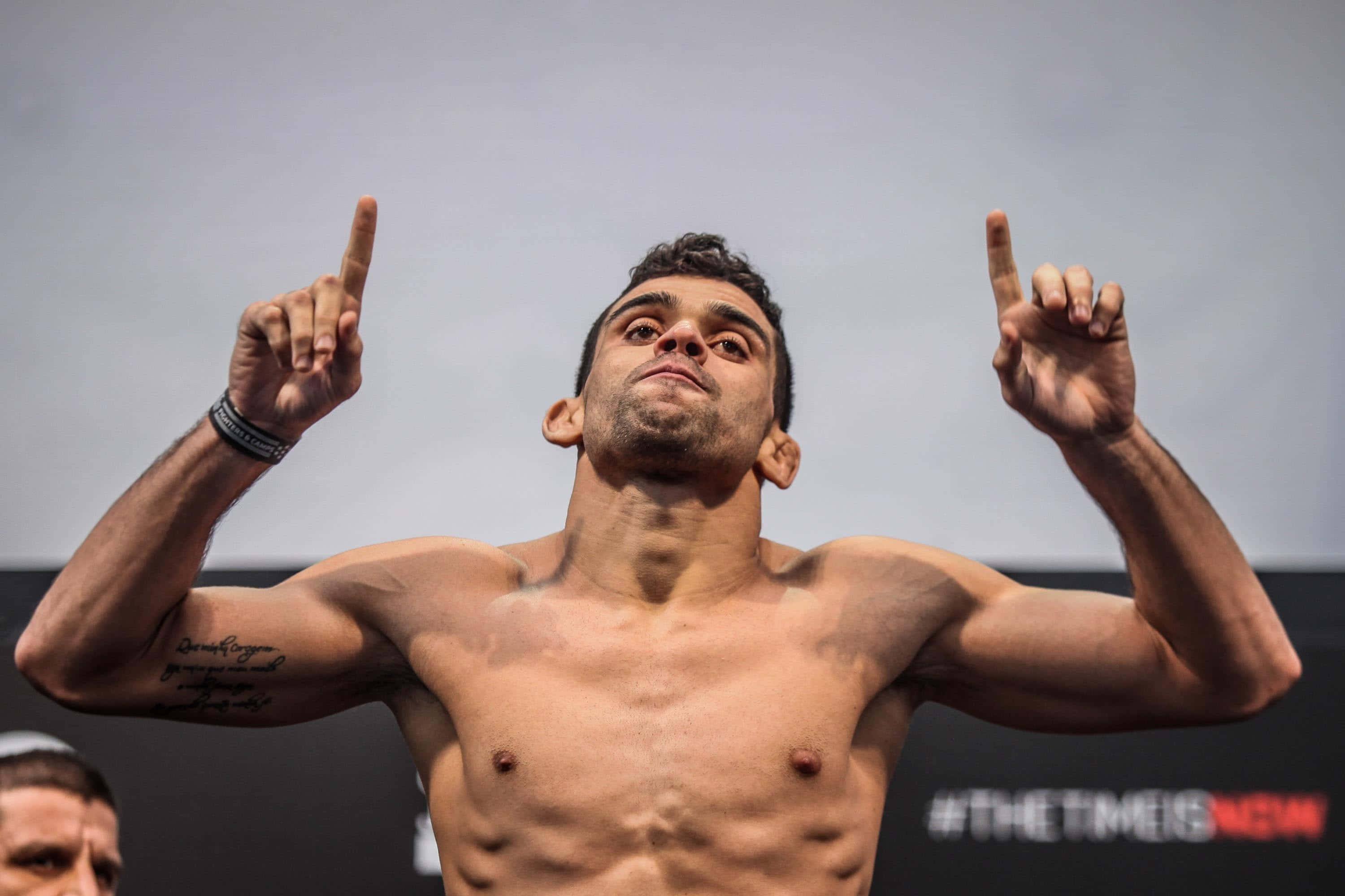 巴西綜合格鬥選手Renan Barão於賽前稱重儀式中舉起雙指 壁紙 — 一名赤膊的肌肉戰士，在樸素背景下，專注地高舉雙食指，展現勝利姿態。