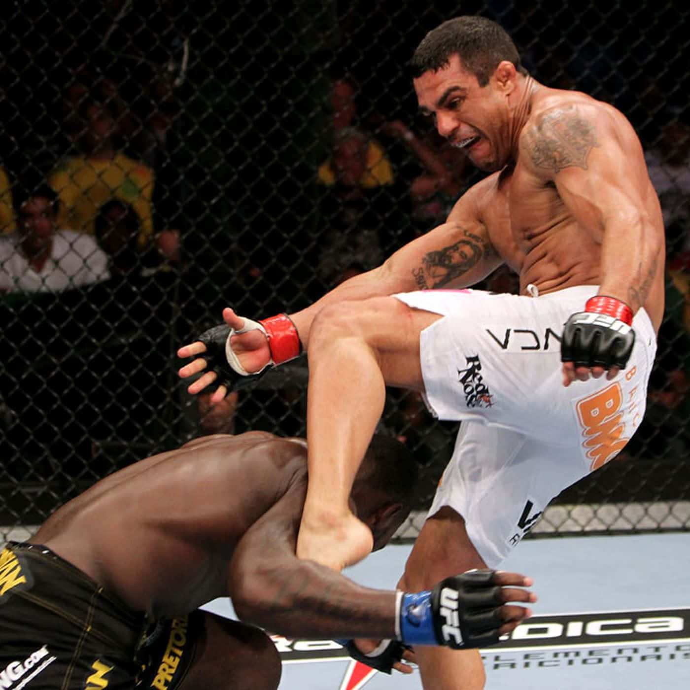 巴西綜合格鬥選手維托·貝爾福特對決安東尼·約翰遜 UFC 142 2012 壁紙 — 一名肌肉發達的拳手在明亮的場館燈光下，於UFC八角籠中向對手踢出一記高踢。