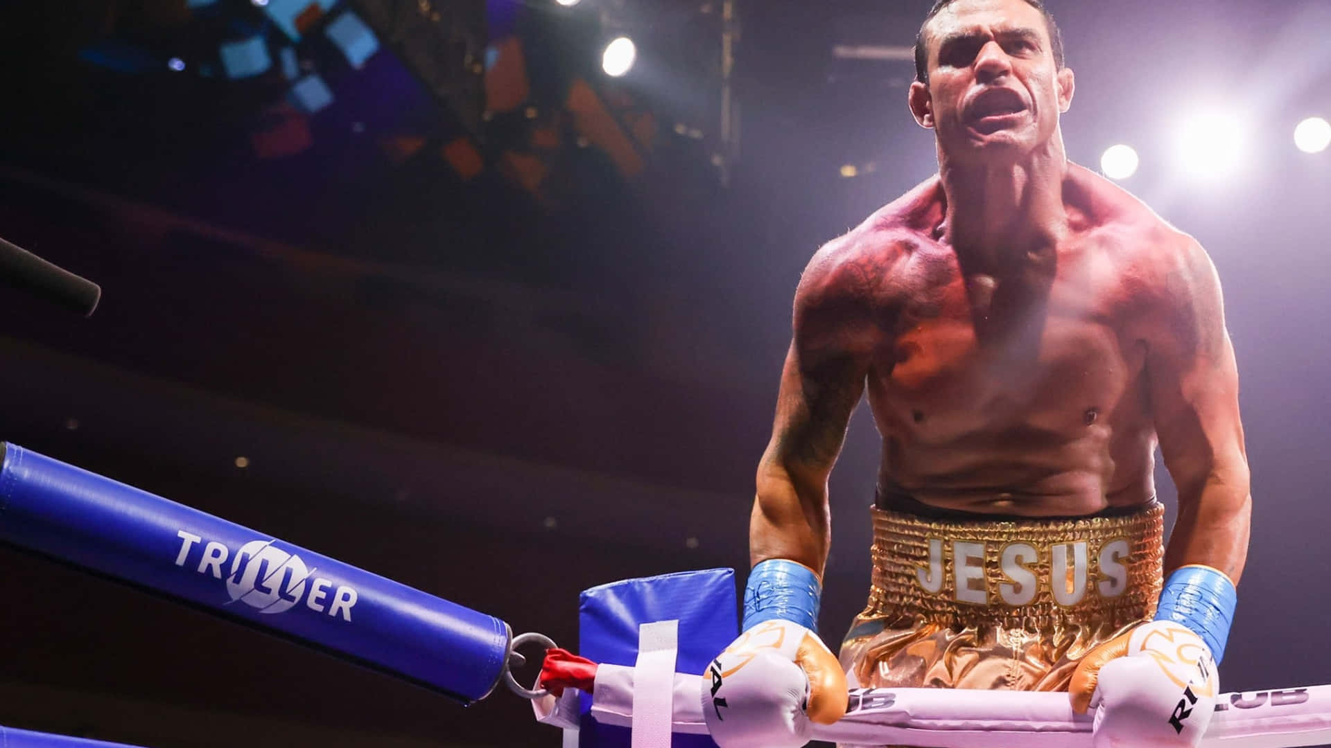 巴西綜合格鬥選手維托·貝爾福特於Triller Fight Club 2021獲勝 壁紙 — 一位肌肉發達的拳擊手穿著金色短褲，在明亮的競技場燈光下靠在擂台繩索上，表情兇猛。