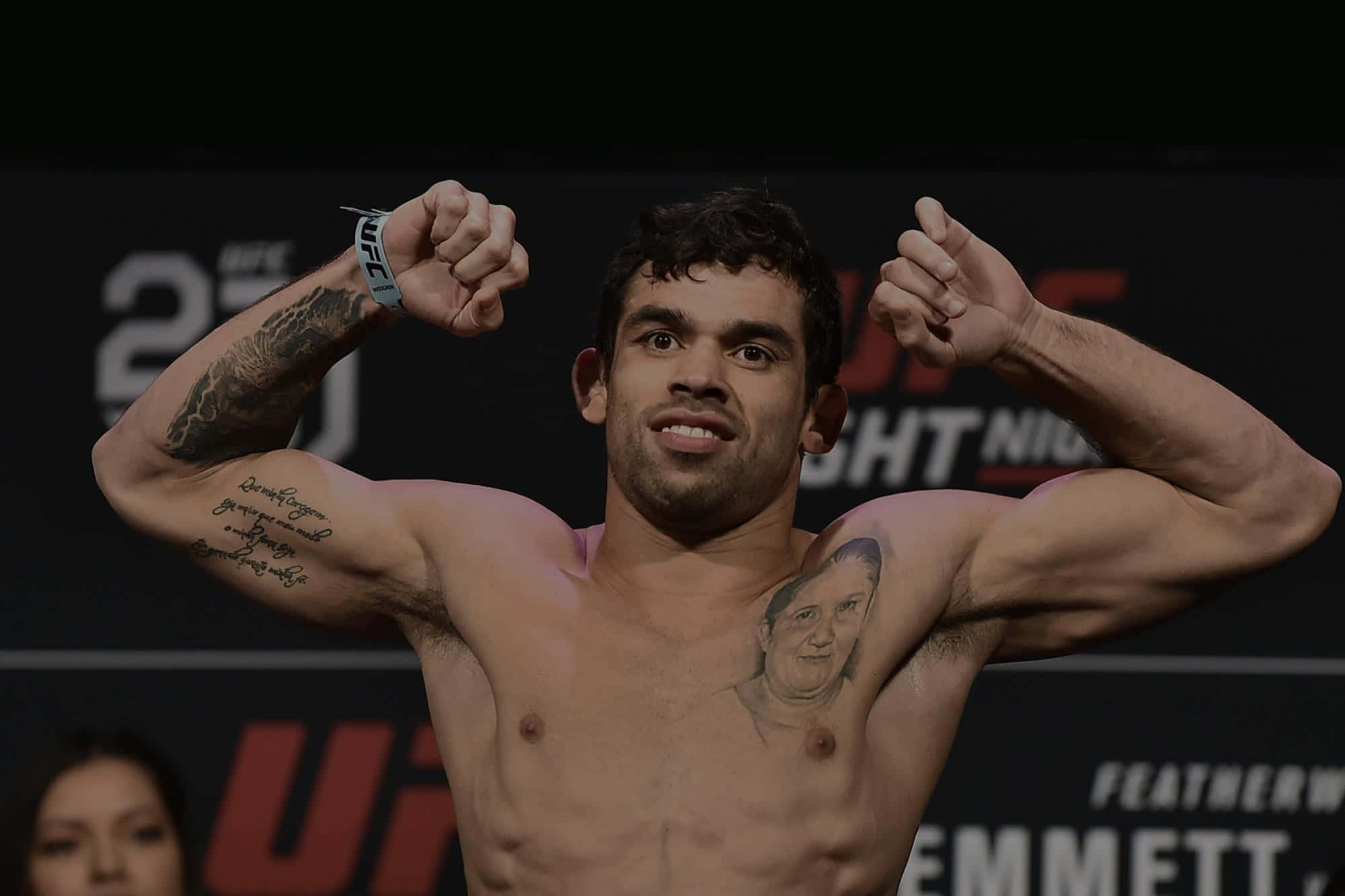 巴西綜合格鬥選手雷南·巴羅稱重時展臂 壁紙 — 一位肌肉發達的UFC拳手在體重磅上屈起手臂，紋身在明亮的場館燈光下清晰可見。