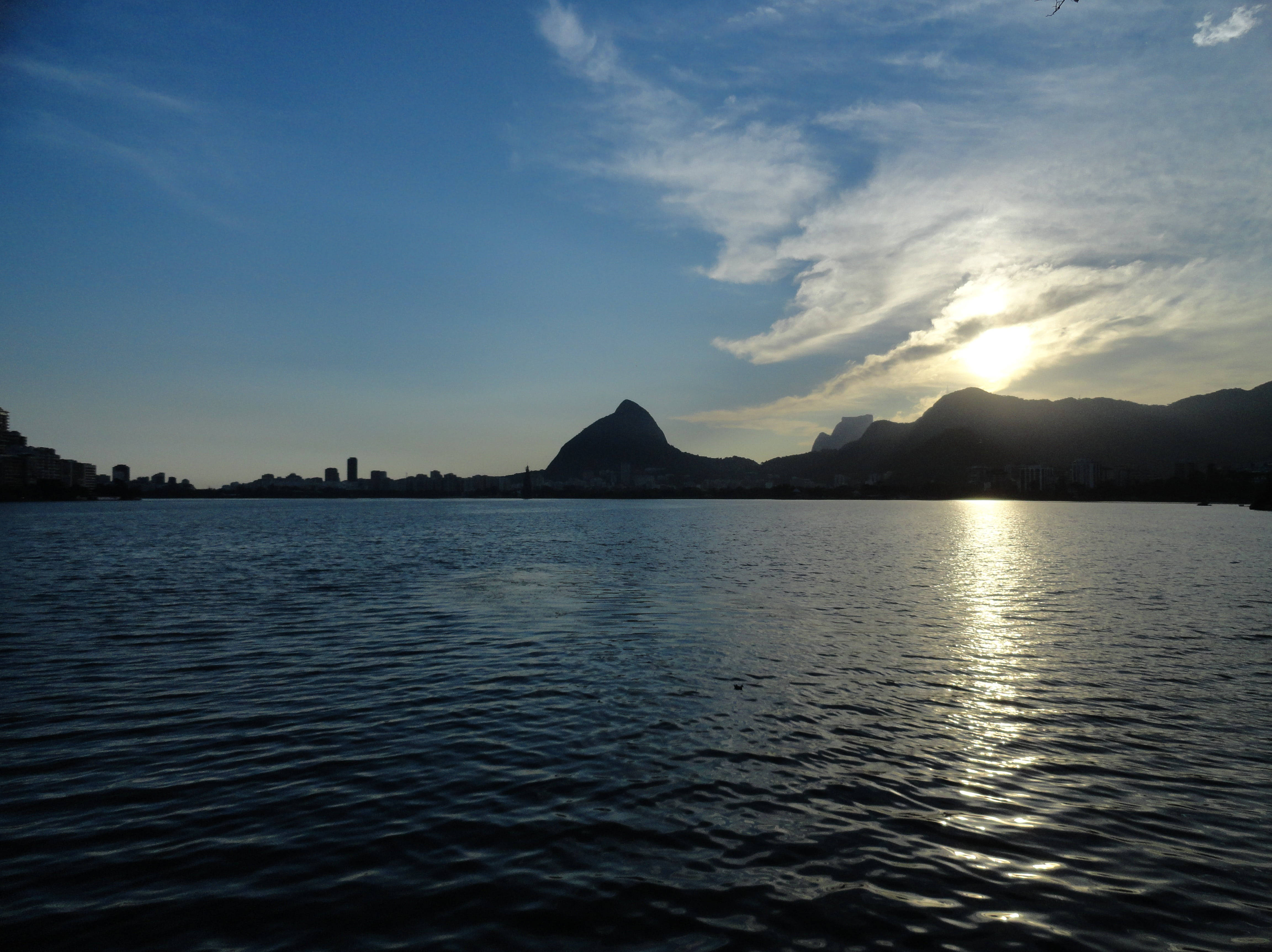 巴西羅德里戈·德·弗雷塔斯潟湖 壁紙 — 夕陽照耀著里約熱內盧標誌性的山脈和水域，城市天際線在藍天下呈現剪影。