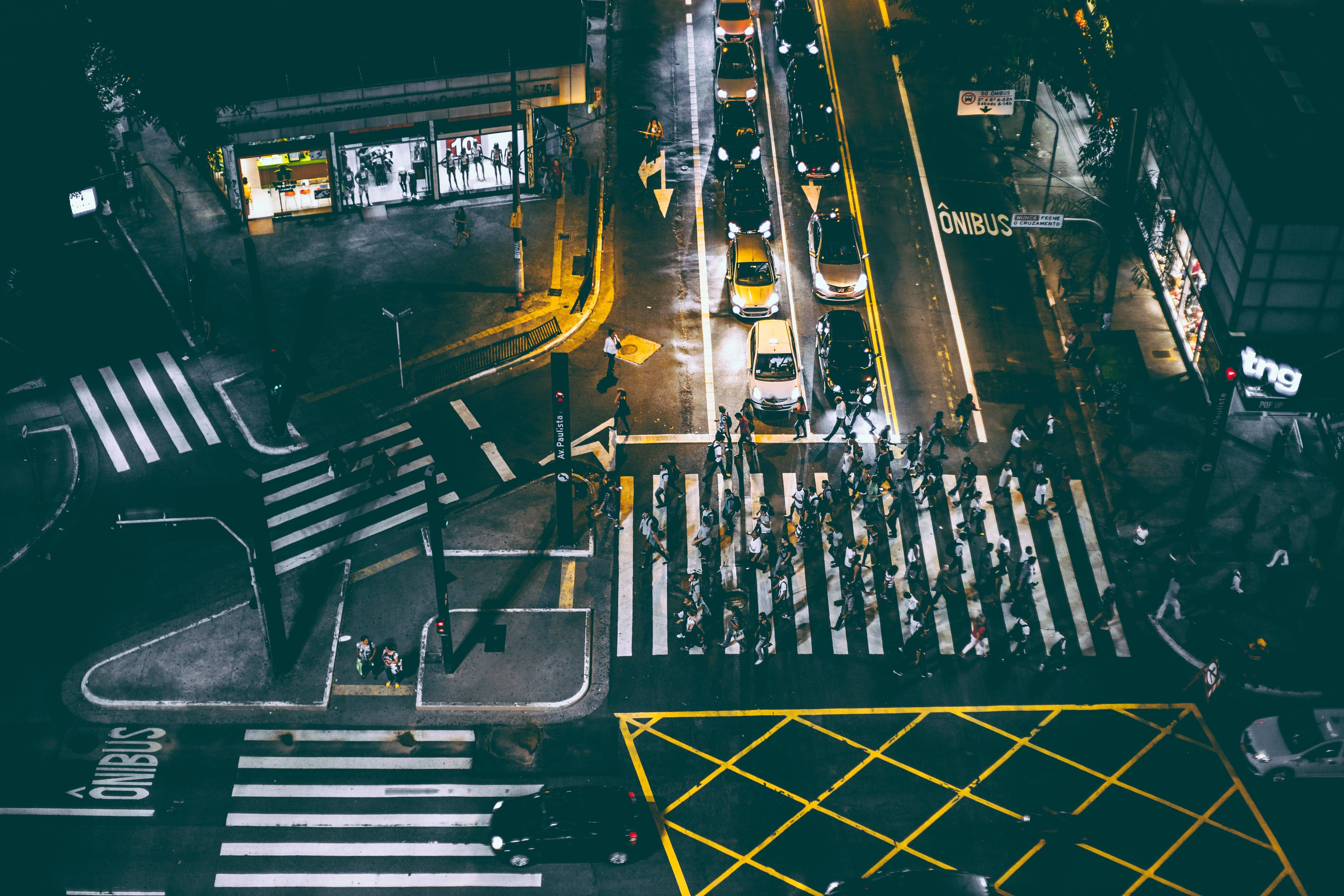 巴西聖保羅空中街景夜間 壁紙 — 夜晚繁忙城市交叉口的鳥瞰圖，行人穿越明亮的白色條紋，汽車在交通中停下。
