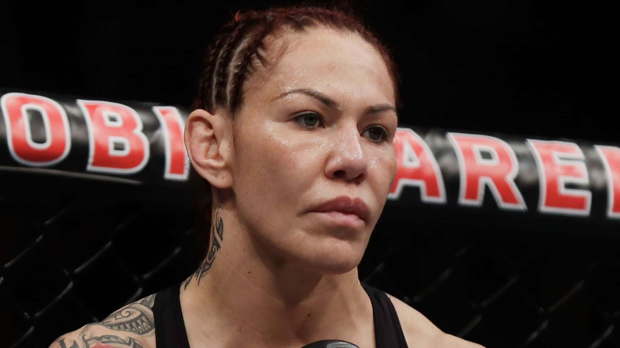 巴西裔美國MMA選手Cris Cyborg Octagon內特寫照 壁紙 — 一位專注嘅女性MMA拳手，身上有紋身，喺明亮嘅場館燈光下喺八角籠內凝視。