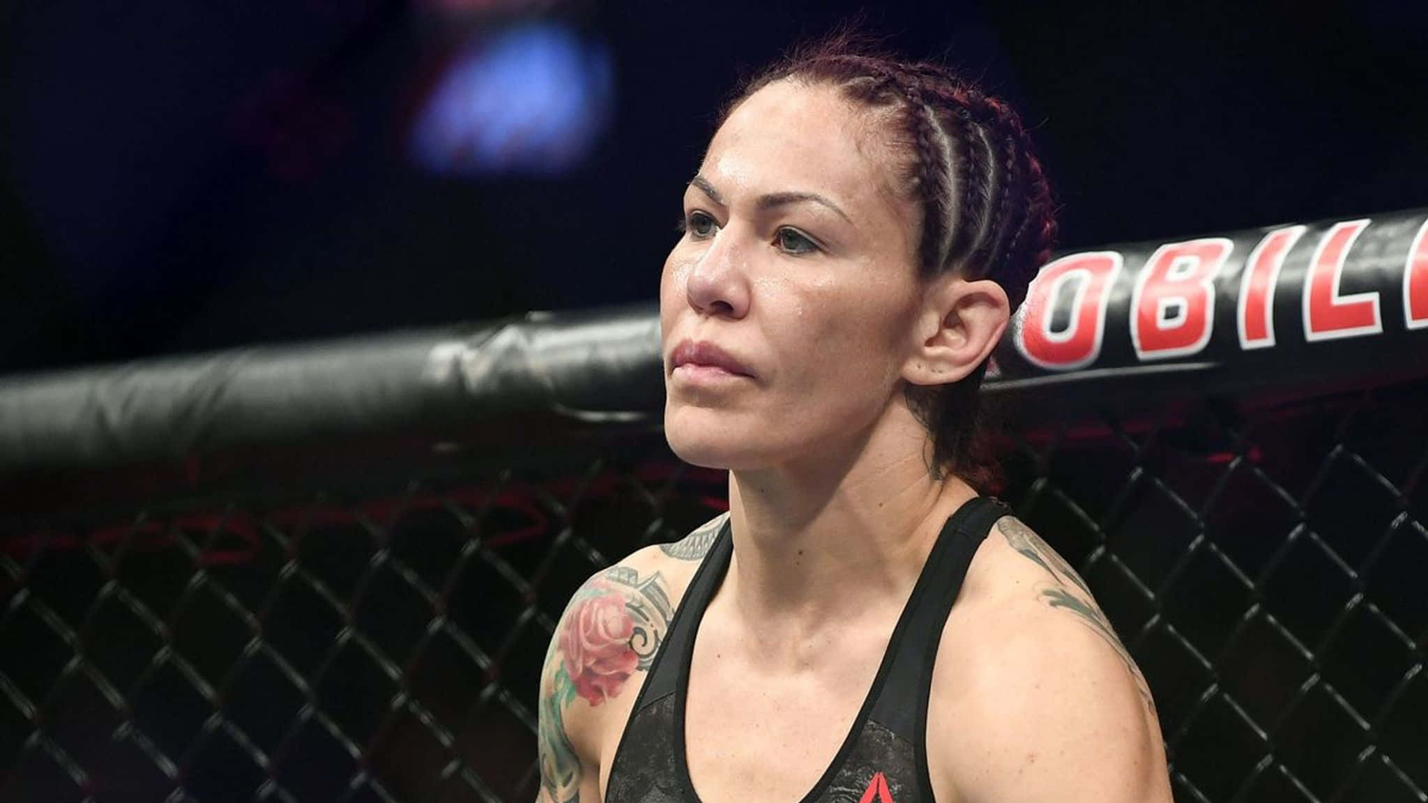 巴西裔美國UFC選手Cris Cyborg側面角度照 壁紙 — 一位專注的女MMA拳手，身上有紋身，在場館燈光下凝視著八角籠內。