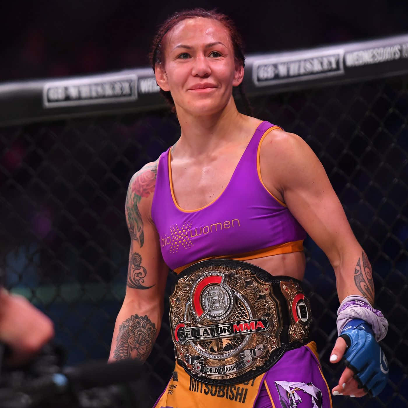 巴西裔美國綜合格鬥選手克莉絲·西伯格2020年獲勝照片 壁紙 — 一位身穿紫色上衣的勝利女性MMA拳手在八角籠內微笑著手持冠軍腰帶。