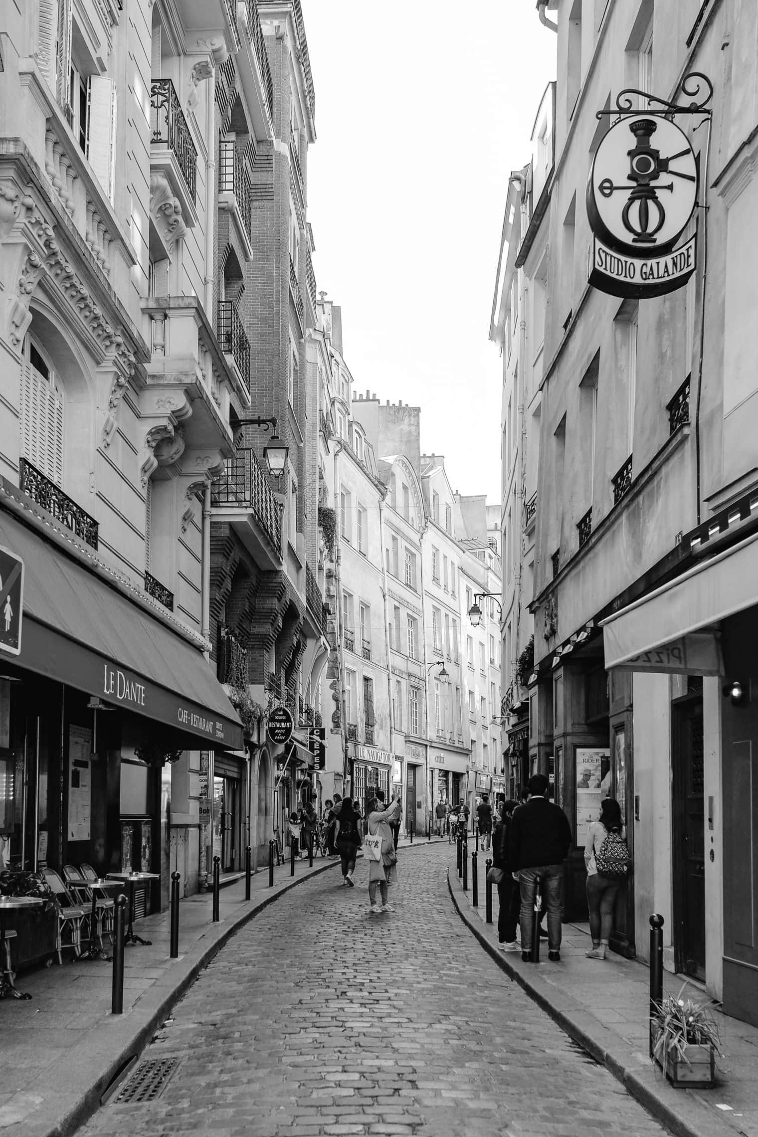Black And White Street 桌布 壁紙 — 巴黎一條狹窄鵝卵石街道的黑白照片，有歷史建築和行人。