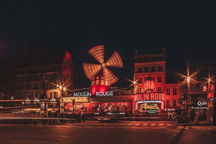  壁紙 — 巴黎紅磨坊的充滿活力的夜景，在黑暗的天空襯托下，紅色霓虹燈和旋轉的風車閃閃發光。