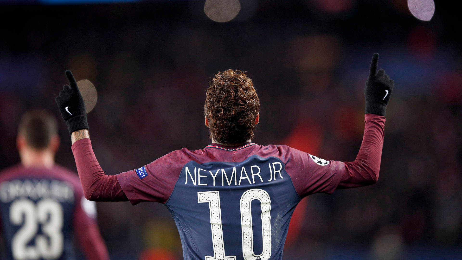 足球運動員尼馬（Neymar Jr）在夜間球場高舉雙臂慶祝。