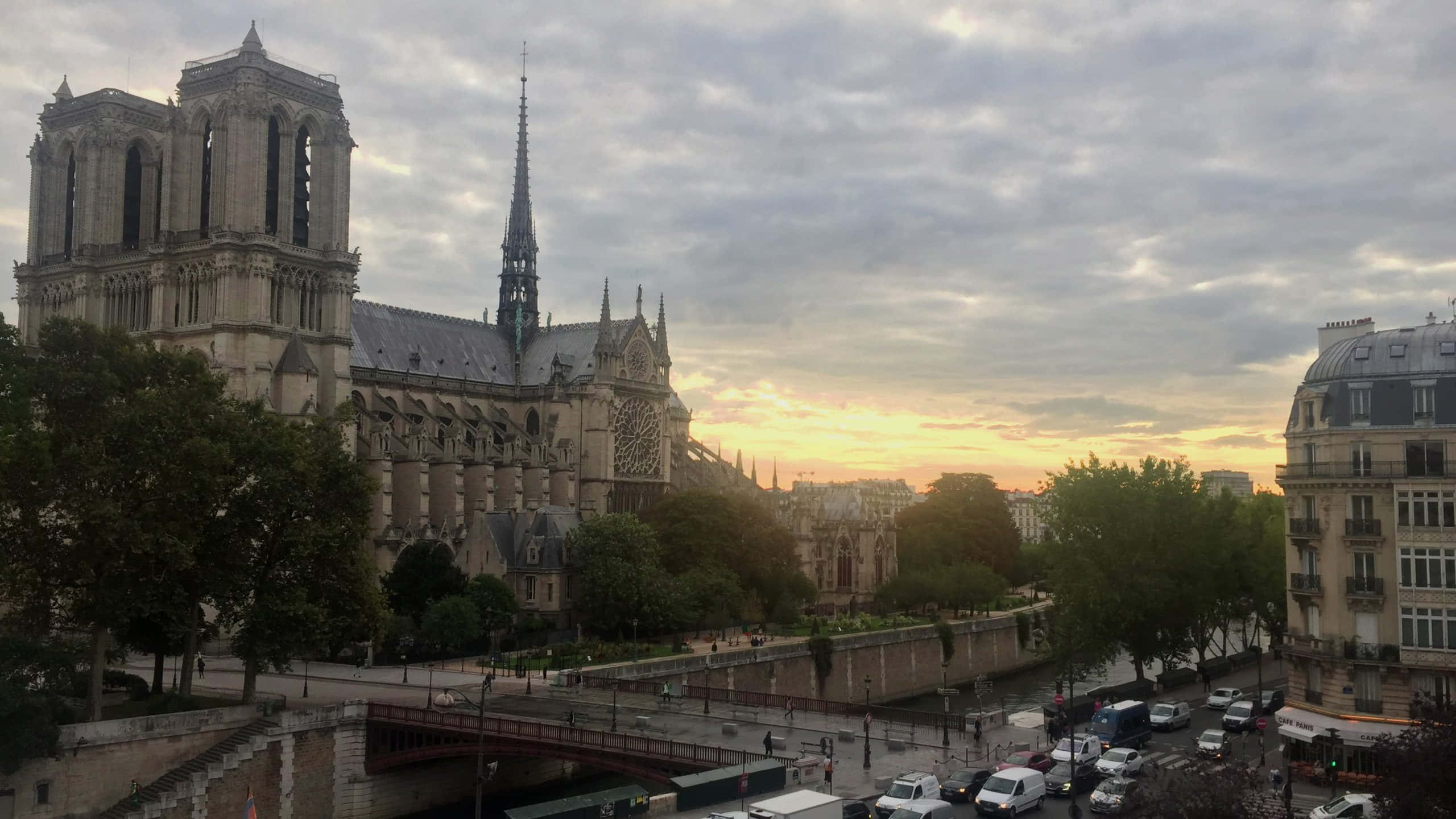 french 桌布 壁紙 — 巴黎聖母院在巴黎屋頂和寧靜河流上空的柔和金色日落天空下巍然聳立。