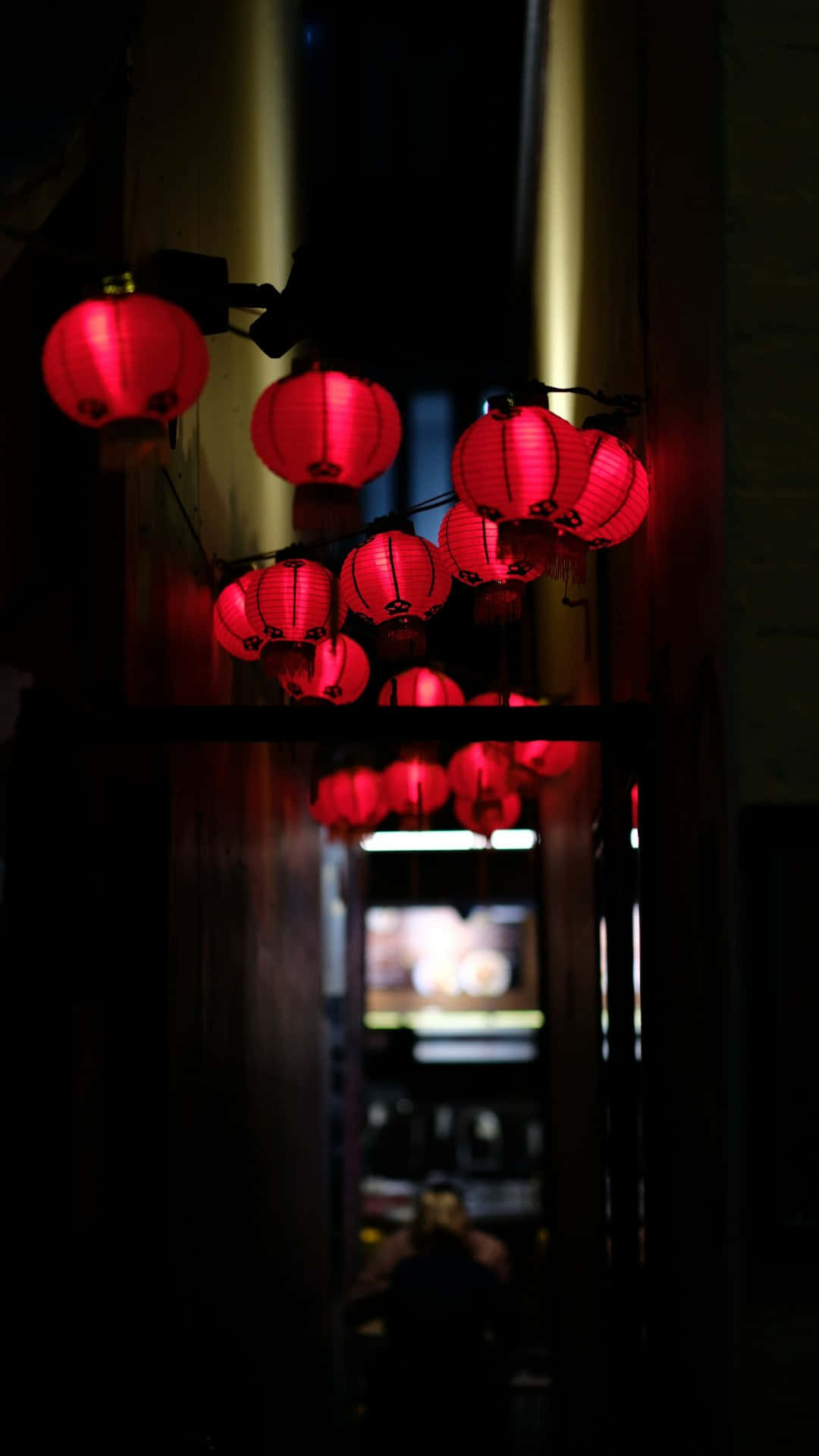 巷弄中的紅燈籠 壁紙 — 發光的紅色紙燈籠懸掛在光線昏暗的小巷中，將溫暖的光線投射在深色木樑上。