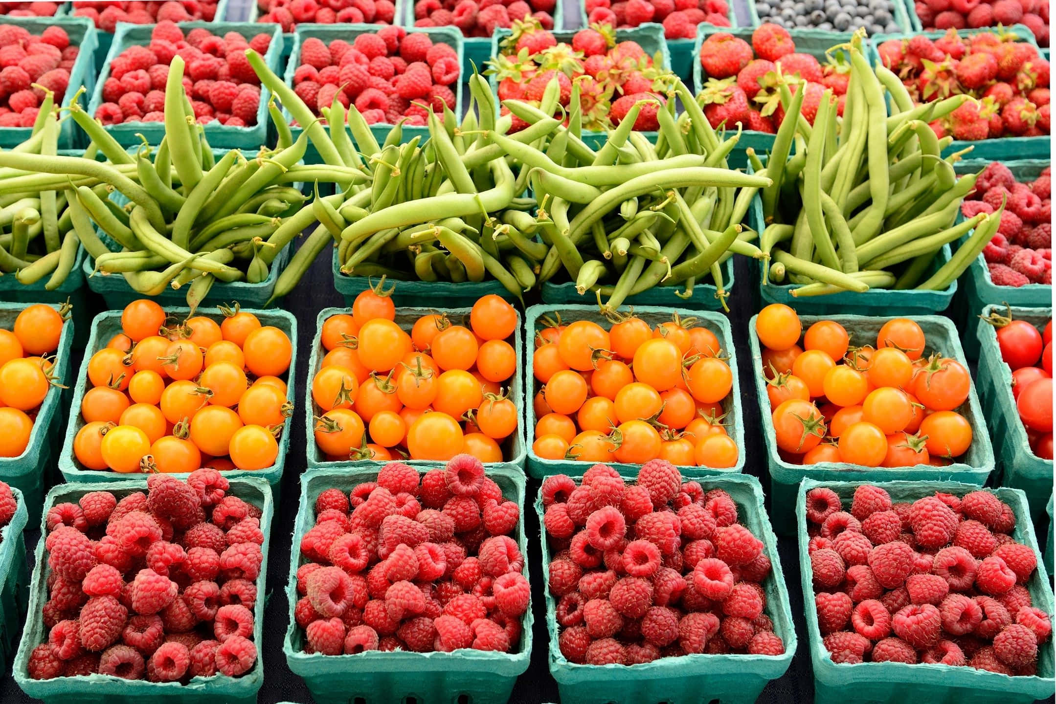 Farmers Market 桌布 壁紙 — 市場中綠色板條箱內新鮮農產品的鮮豔展示，包括青豆、橙色車厘茄和紅桑子。