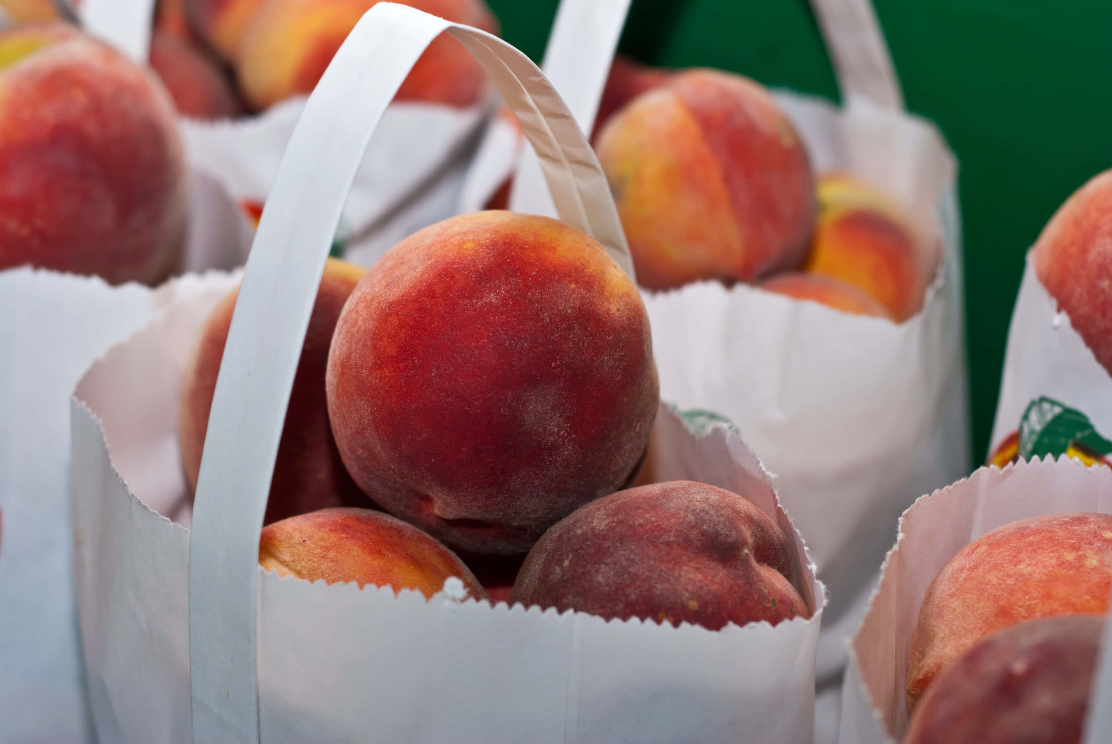 Summer Fruits 桌布 壁紙 — 市場攤位上，白色紙袋裡裝著多汁成熟的桃子，紙袋有手柄。