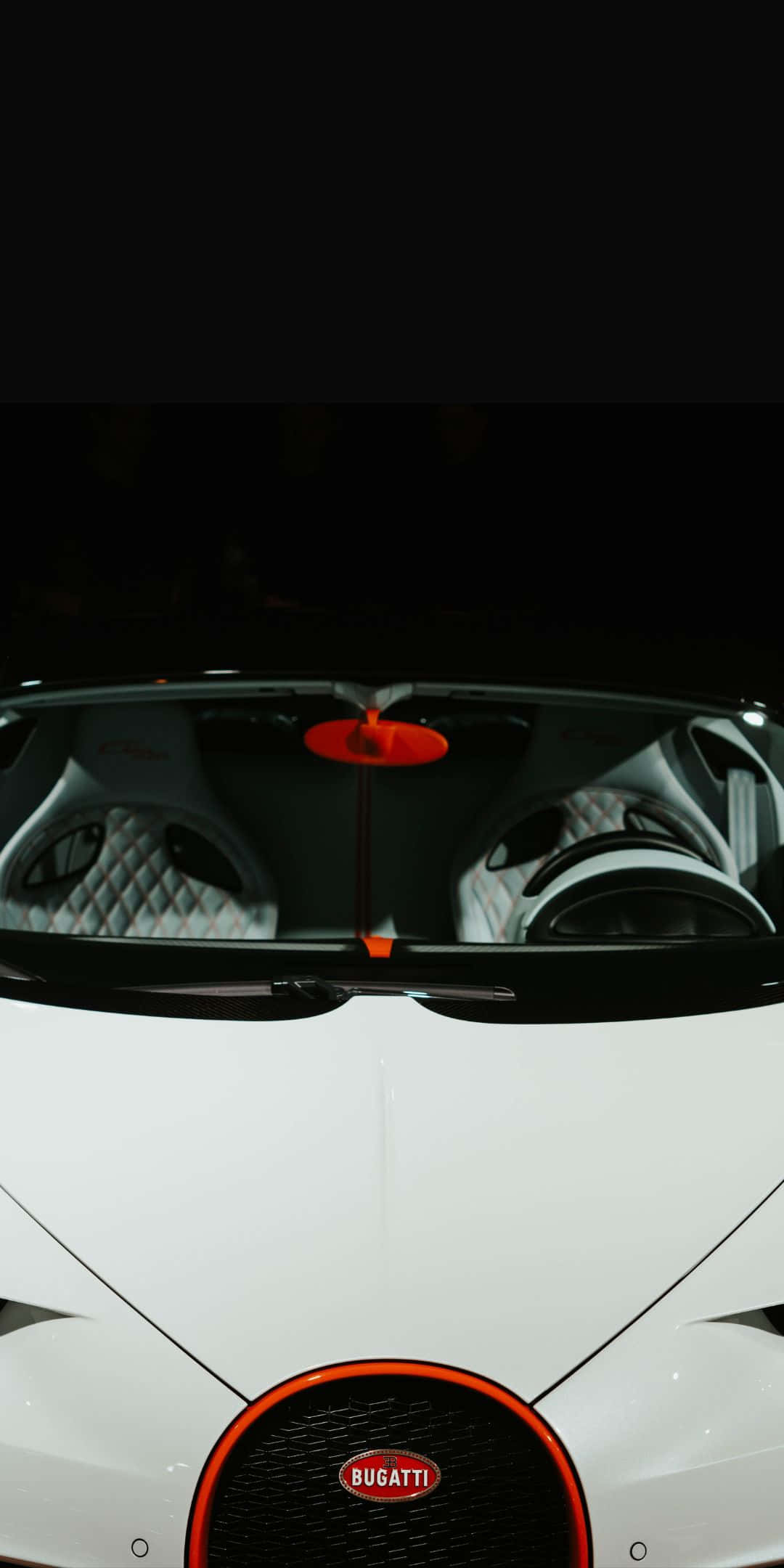 布加迪Chiron前外觀像素3背景 壁紙 — 白色Bugatti超級跑車的俯視圖，帶有橙色點綴和黑色菱格紋座椅，在戲劇性燈光下。