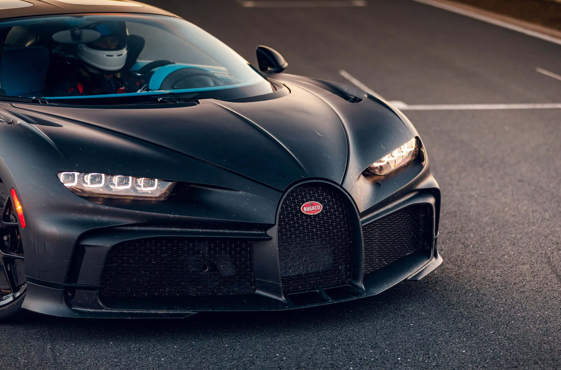 啞光黑色Bugatti Chiron，司機戴著頭盔，在日落時分的瀝青路上。